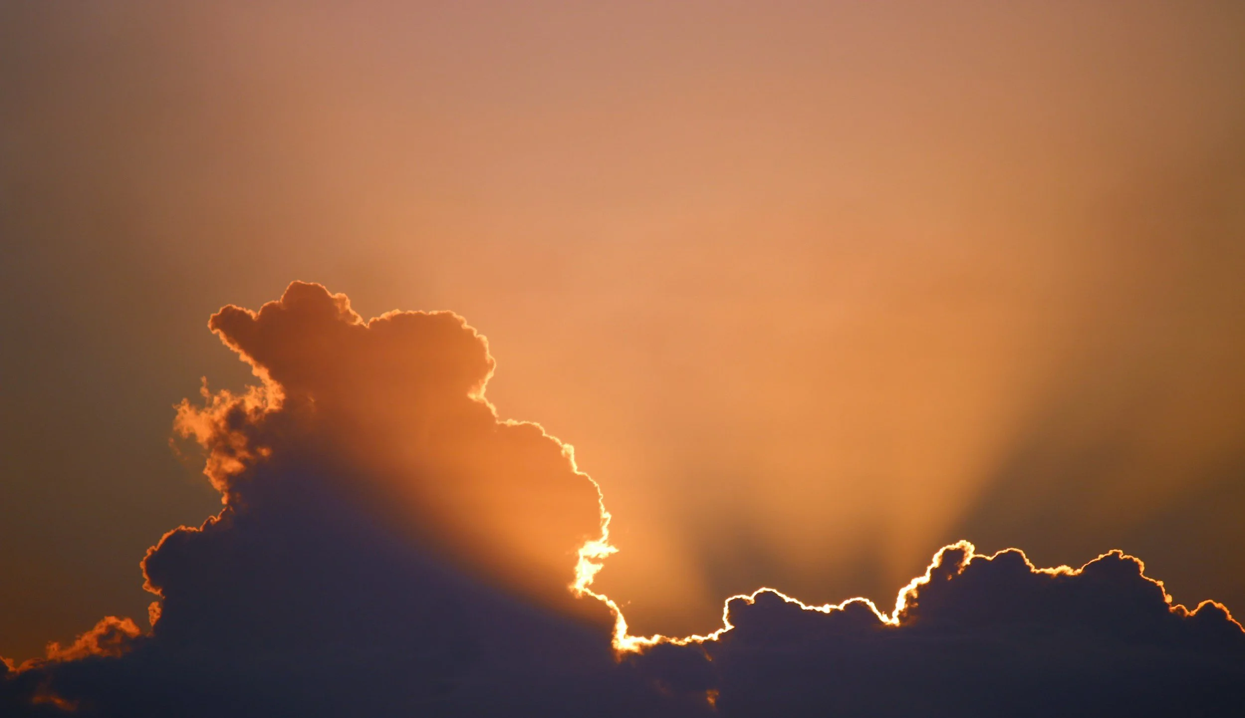 Sunset sky with clouds, some illuminated orange and gold.