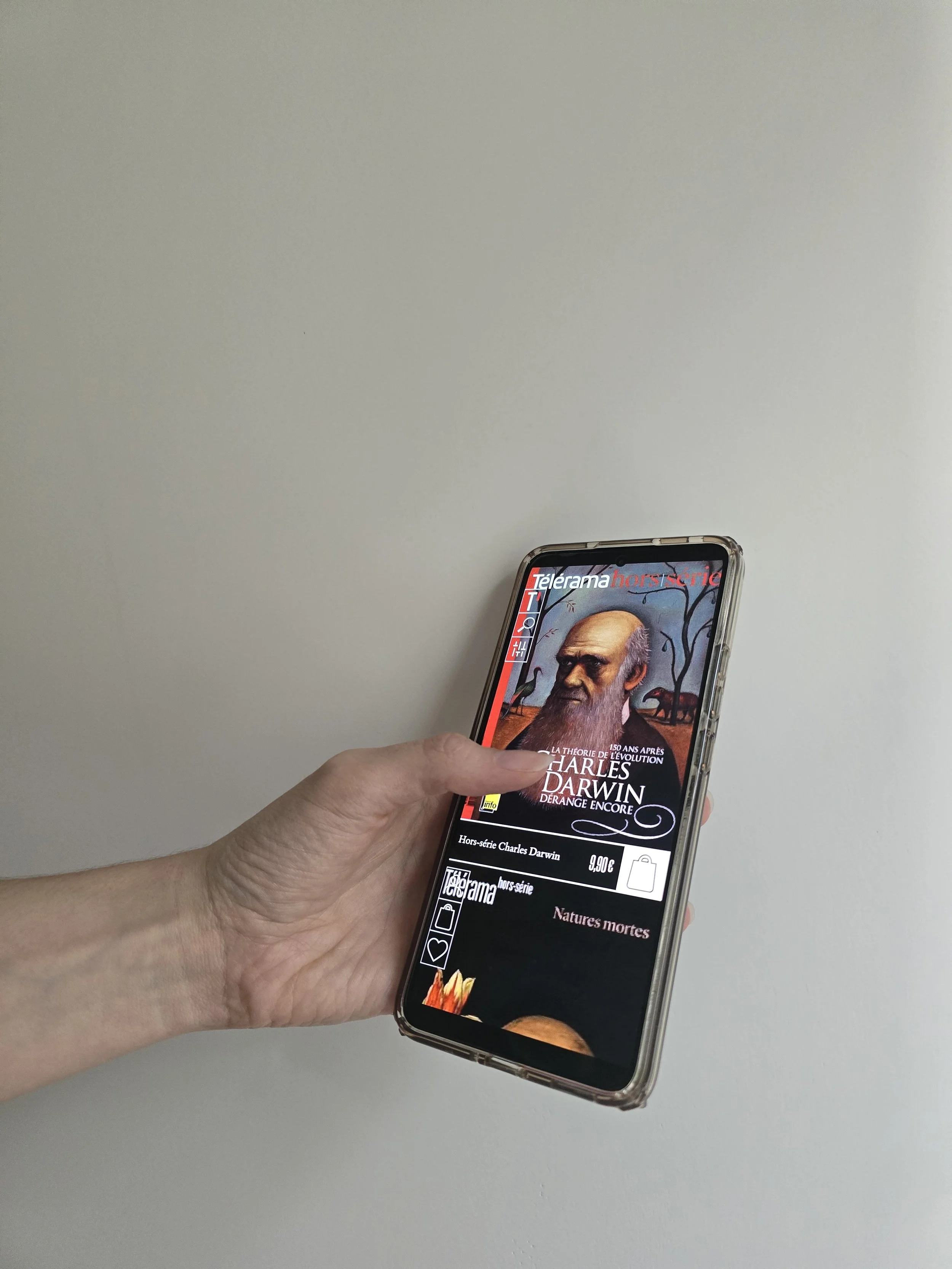 Une main tient un téléphone portable affichant une page de vente pour un livre sur Charles Darwin, avec une image d'un portrait de Darwin sur fond noir.