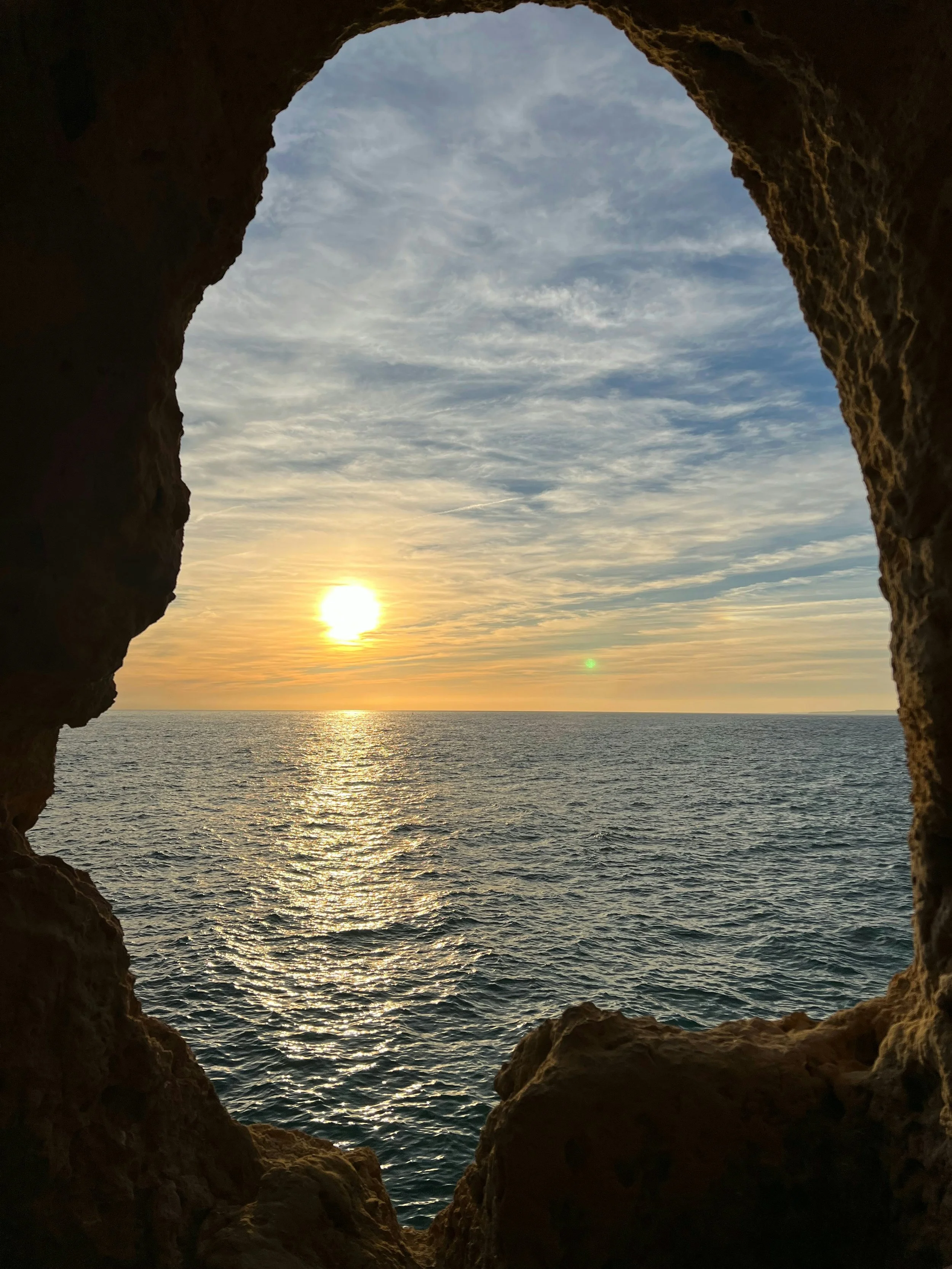 Sunset over the ocean viewed through a rocky opening or cave.