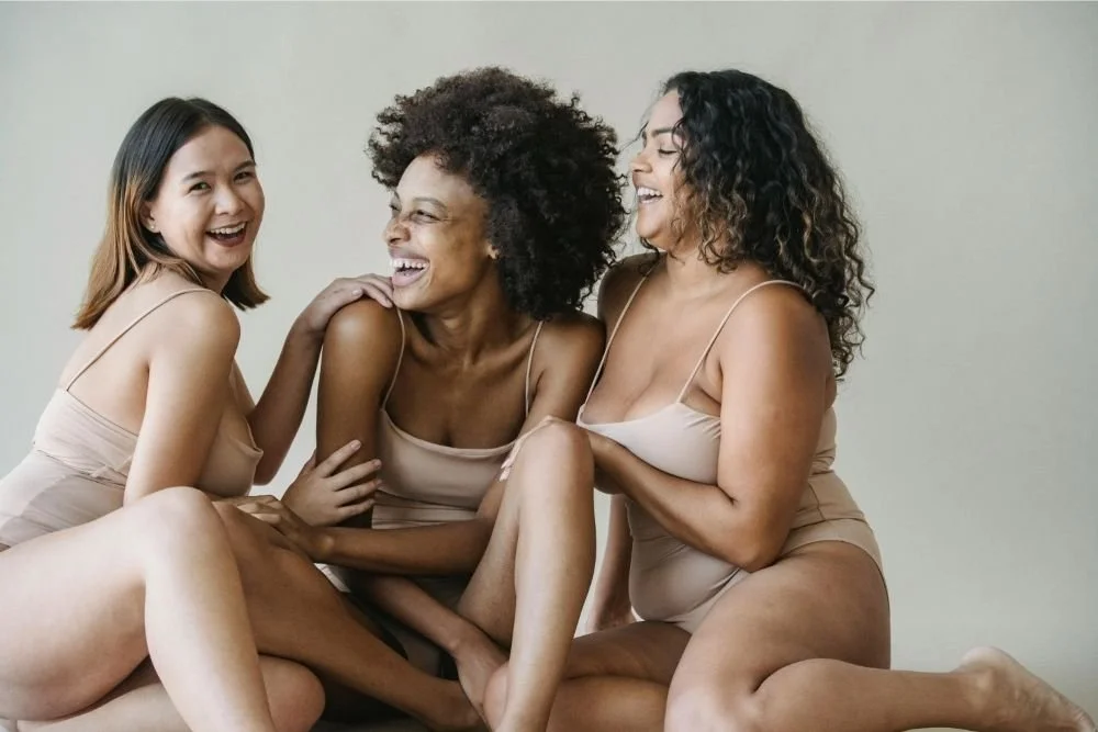 Three women of different ethnicities sitting together, smiling and laughing.