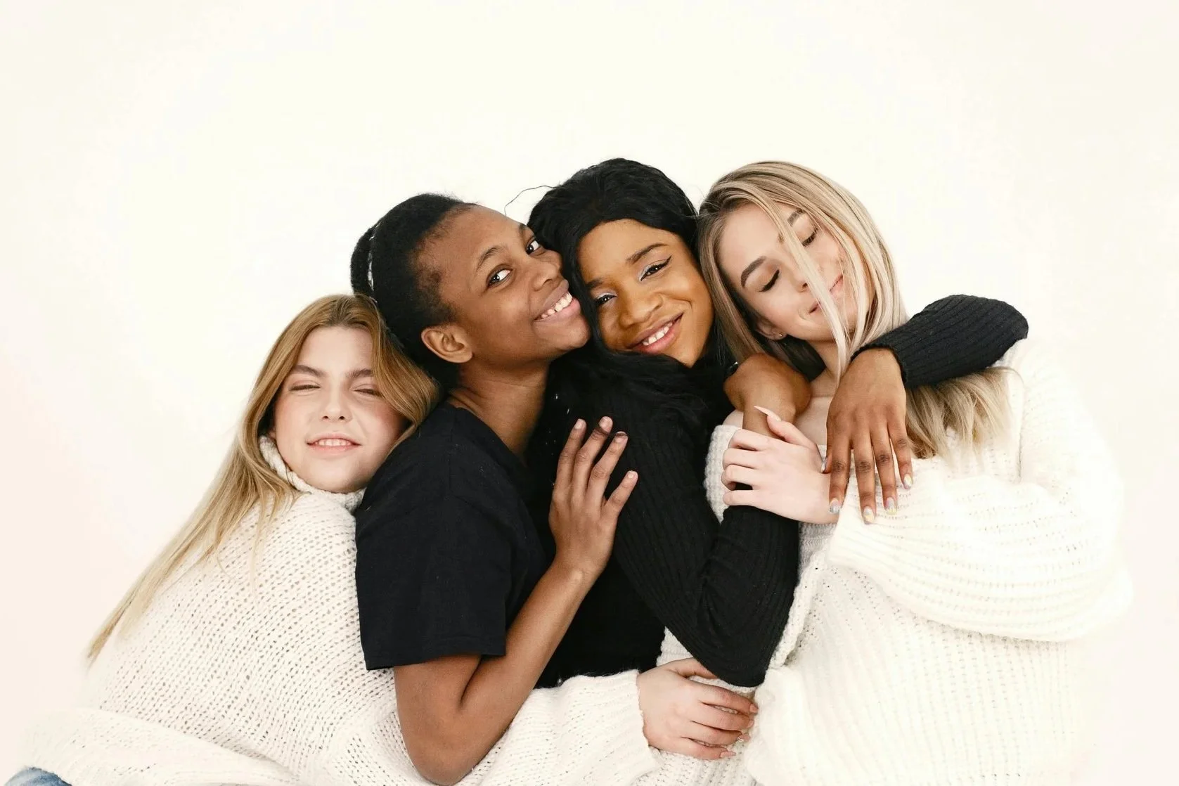 Four women hugging and smiling against a white background.