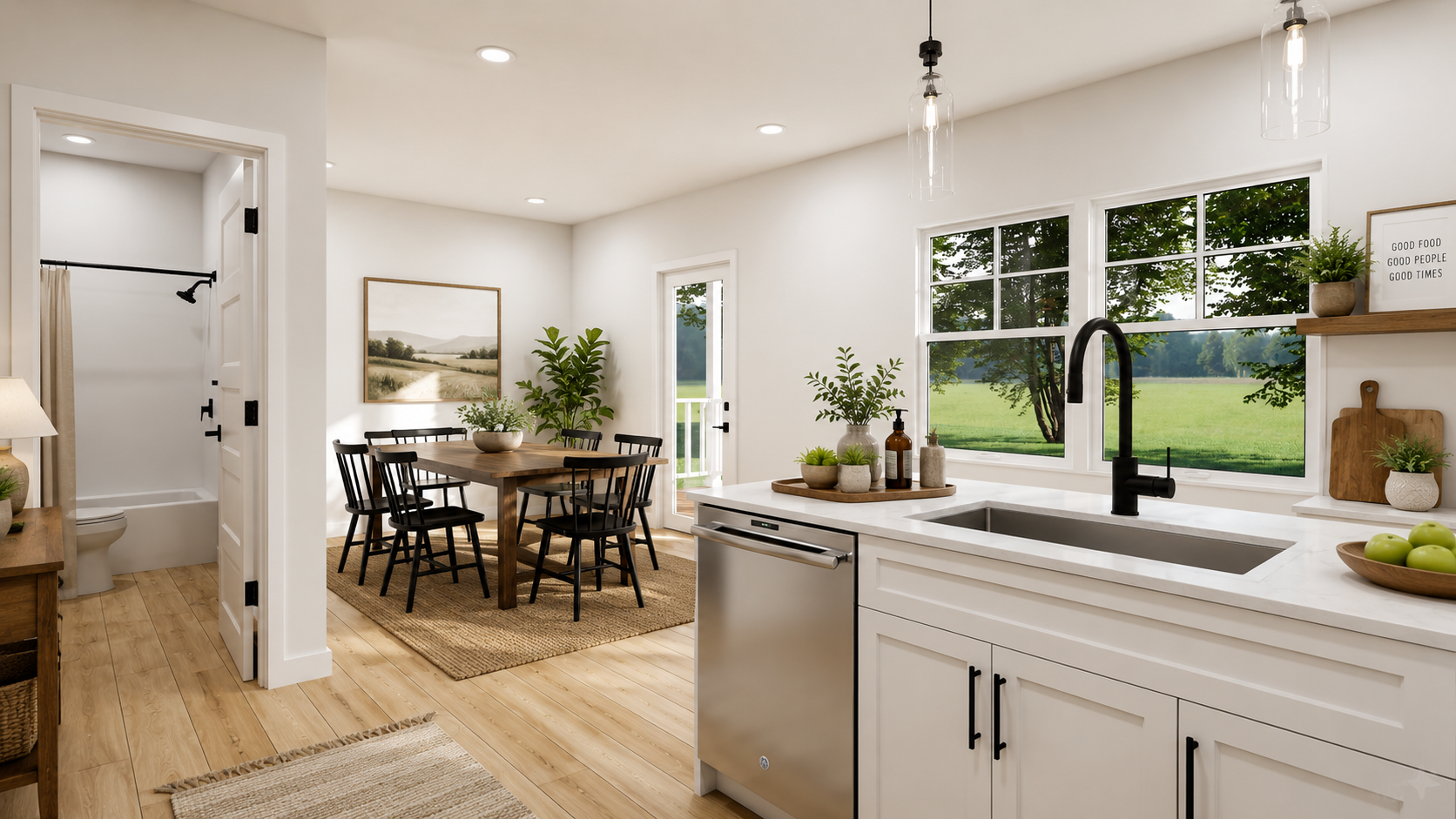 Bright kitchen and dining area with white walls, black window frames, a wooden dining table with six black chairs, and a view of a green outdoor field through large windows. The kitchen features white cabinets, a black faucet, a white countertop, and decorative plants. Visible in the background is a small bathroom with a toilet and shower with a tan shower curtain. Sunlight streams through the windows, creating a warm atmosphere.