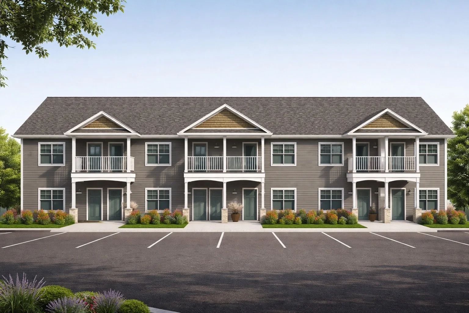 A modern, two-story apartment building with three sections, gray siding, white trim, and small balconies on the second floor. There are parking spaces in front and landscaped bushes and flowers along the building.