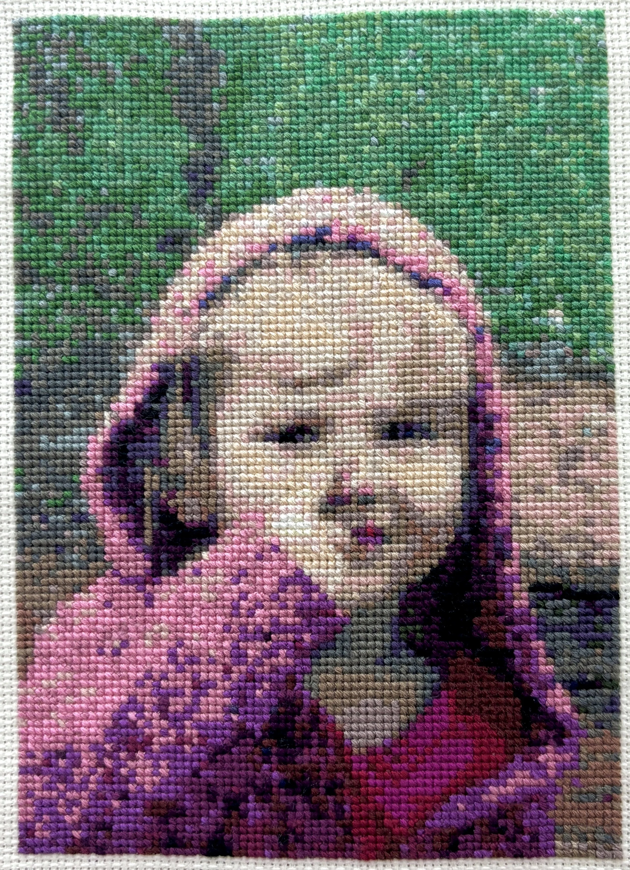 Cross-stitch embroidery of a child with blonde hair, wearing a pink top, set against a green background.