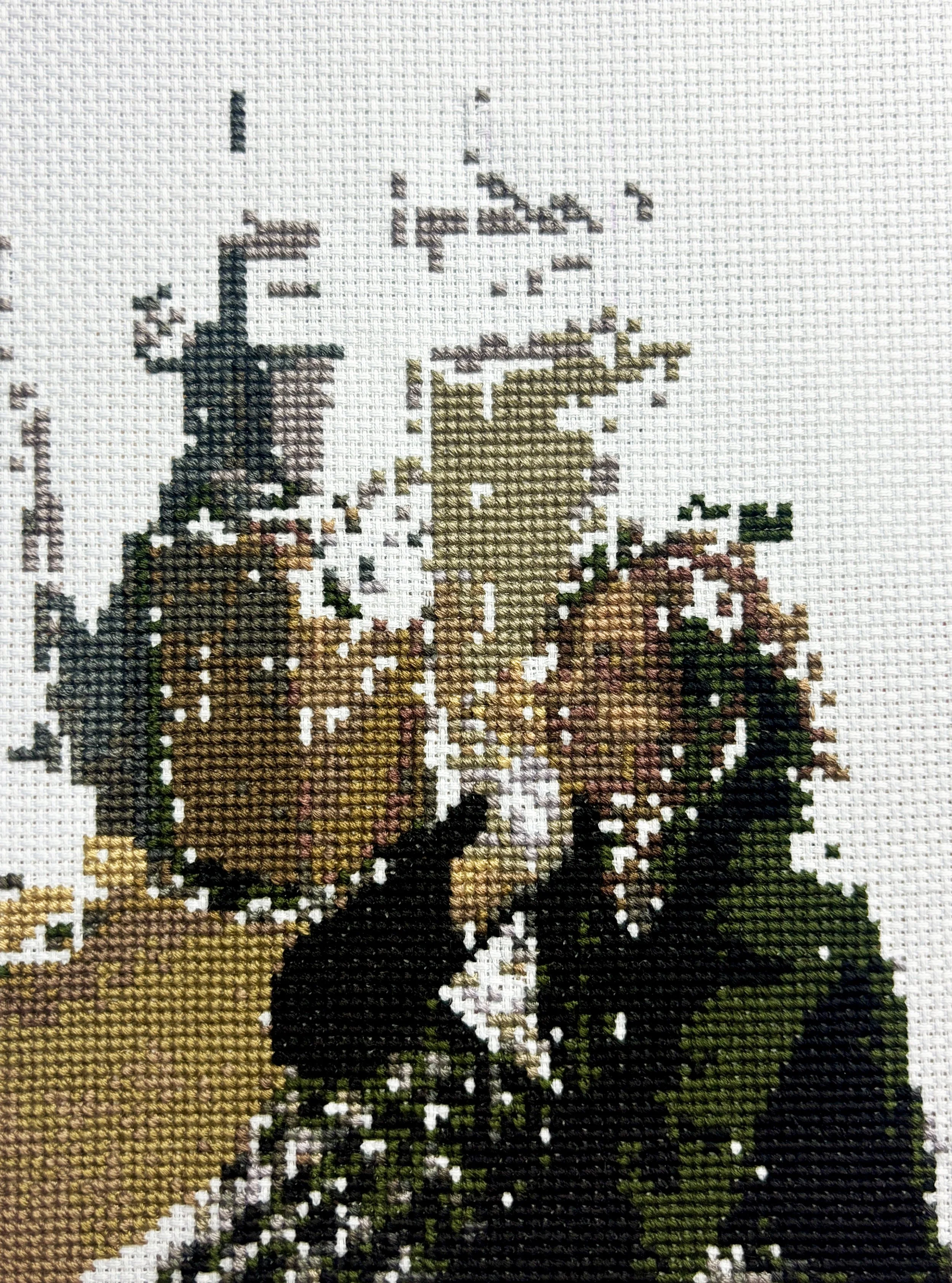Close-up of a cross-stitch embroidery depicting a person sat in a hospital bed.