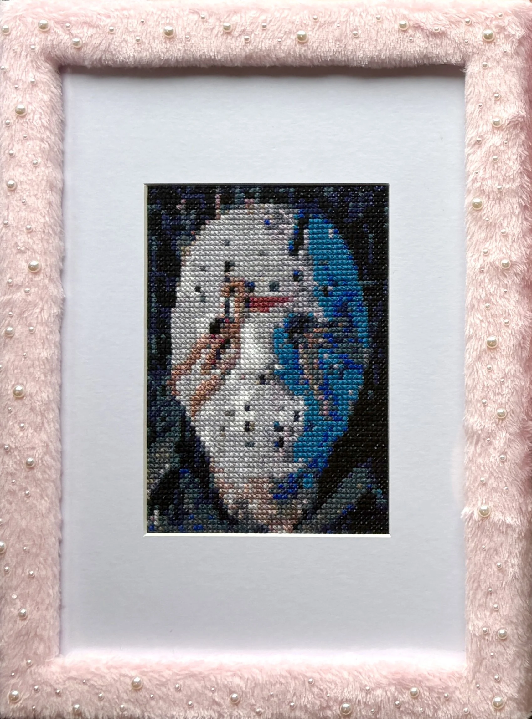 Cross-stitched portrait of a horror character framed in pink faux fur decorated with pearls.