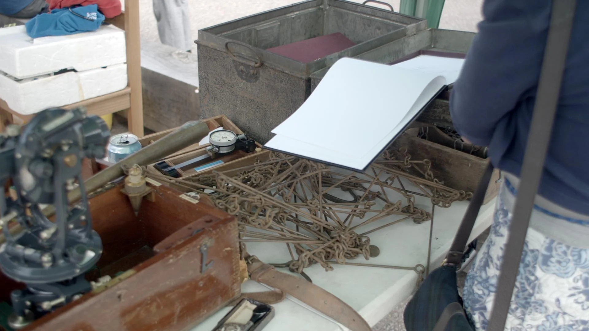Historical iron surveyor's measuring chains displayed alongside vintage surveying equipment and an open logbook on a table.
