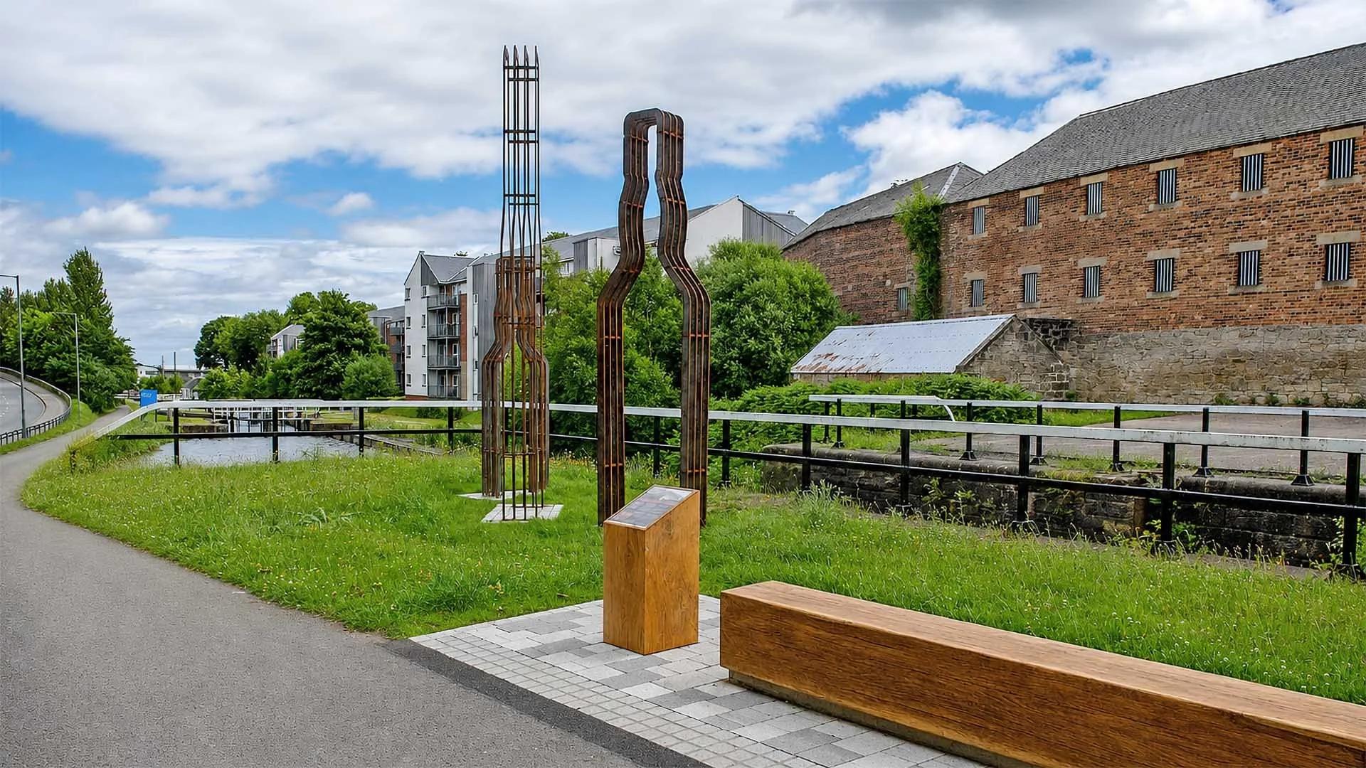 Large metal bottle sculptures alongside a towpath seating area at Rosebank Distillery, next to the Forth and Clyde Canal.
