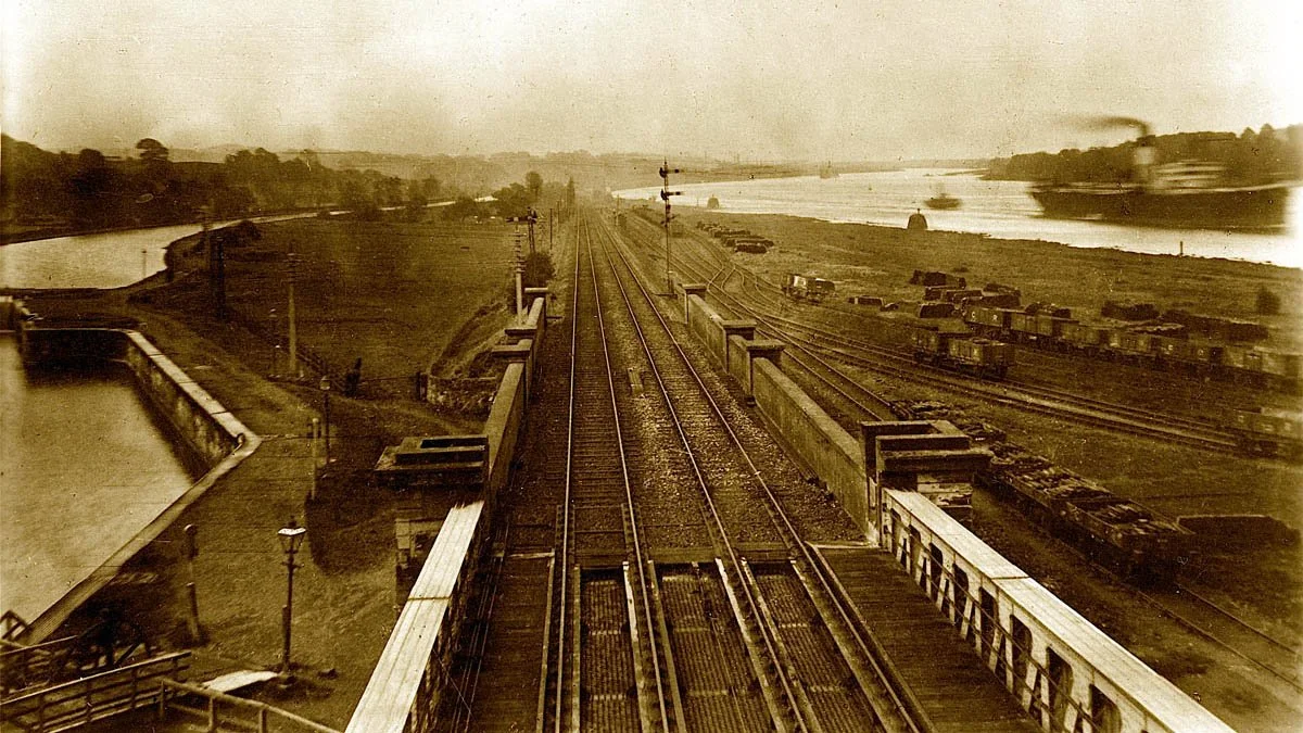 A vintage sepia-toned photograph looking along railway tracks on a bridge towards Bowling Harbour, with canal locks to the left and steamships on the River Clyde to the right.