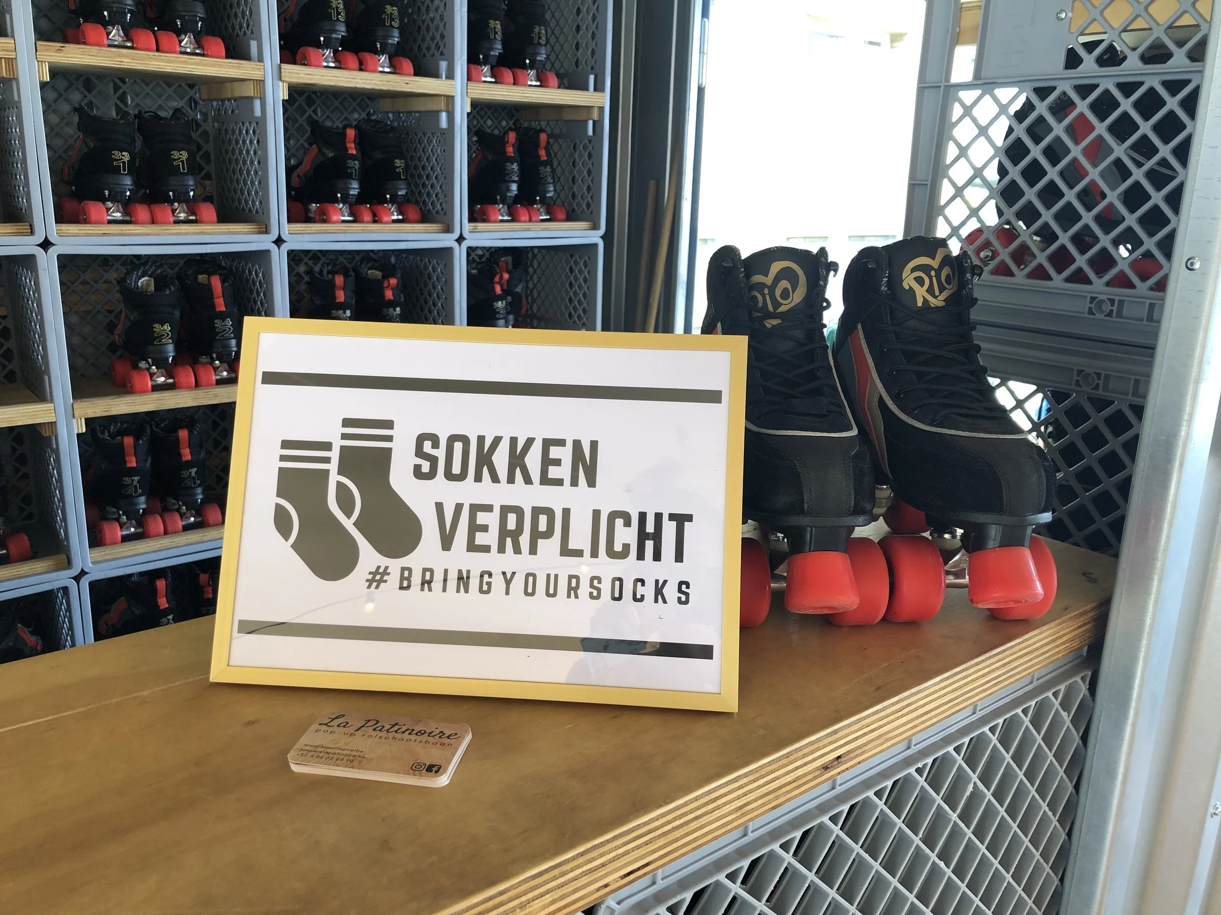 A shelf with multiple pairs of roller skates and a sign in front that says 'Sokken Verplicht' and '#Bringtoyourocks'.