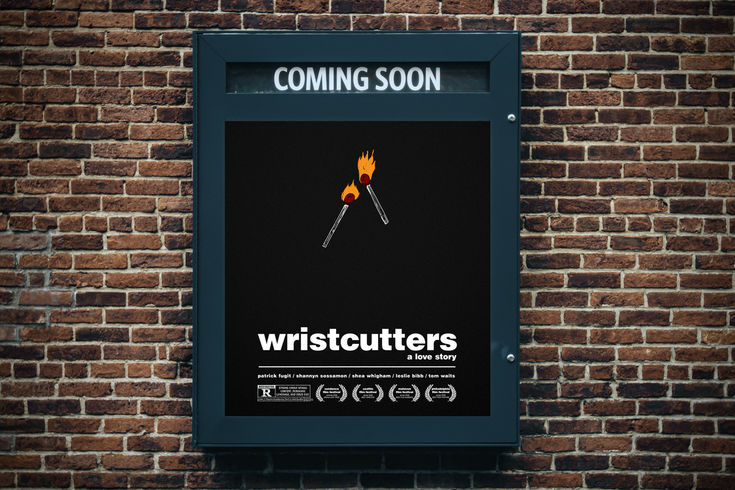 A poster on a brick wall advertising the movie "Wristcutters: a love story" with two matchsticks on fire and the text "Coming Soon" at the top.