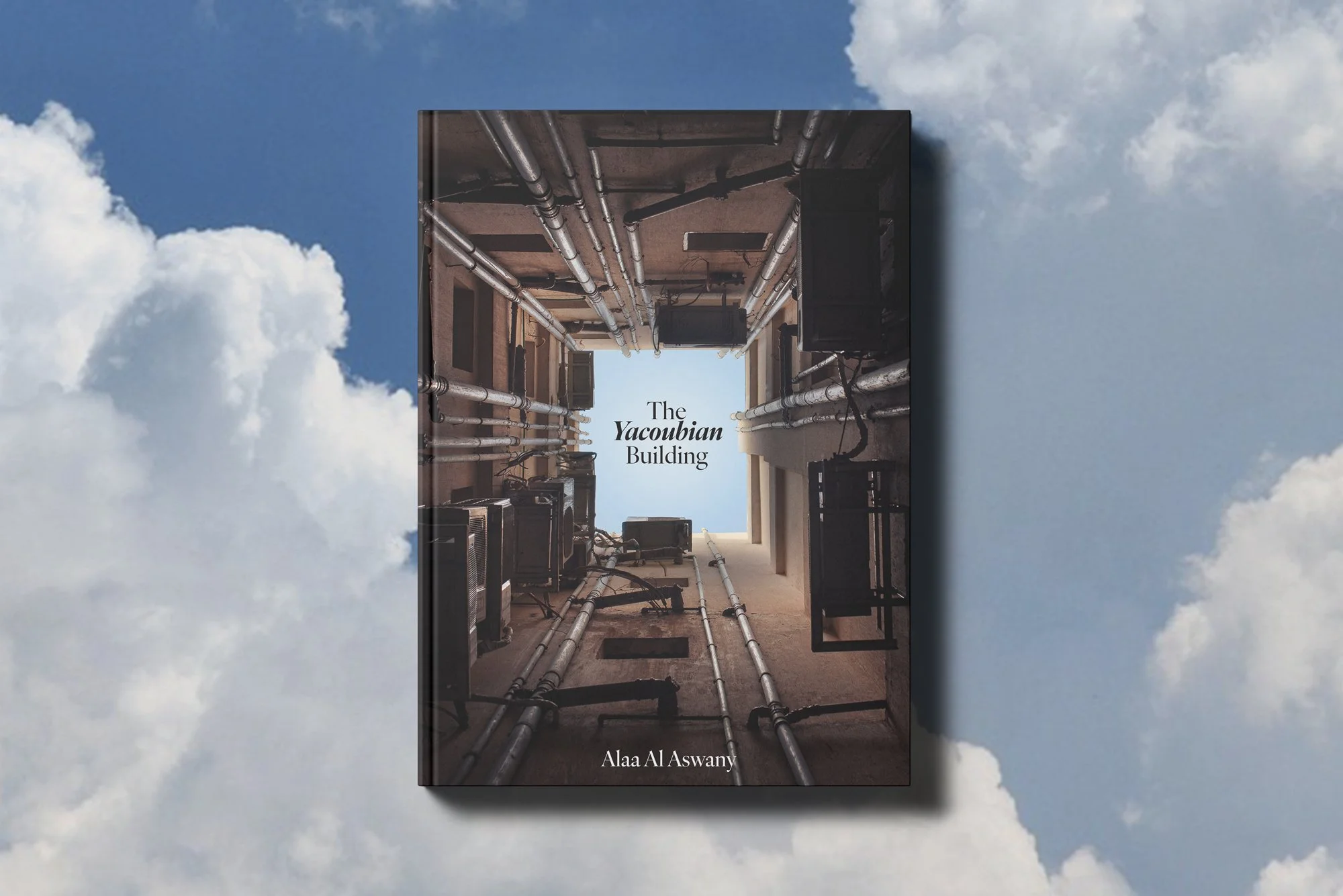 Book titled 'The Yacoubian Building' by Alaa Al Aswany showing an upward view of a building's interior with pipes and air conditioning units on the ceiling.