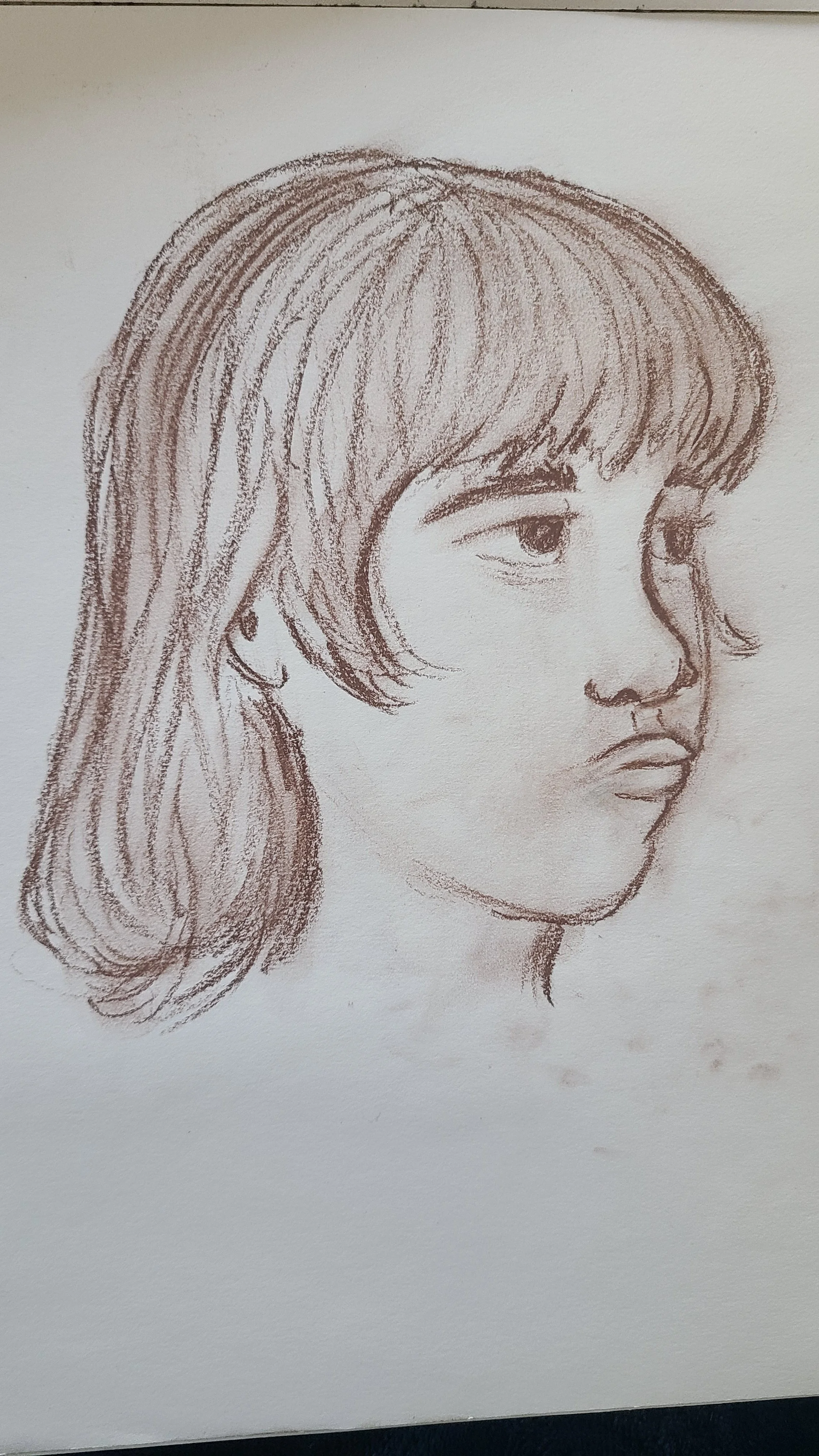 A pencil sketch of a woman's face in profile facing right, with long hair, defined eyebrows, and full lips.