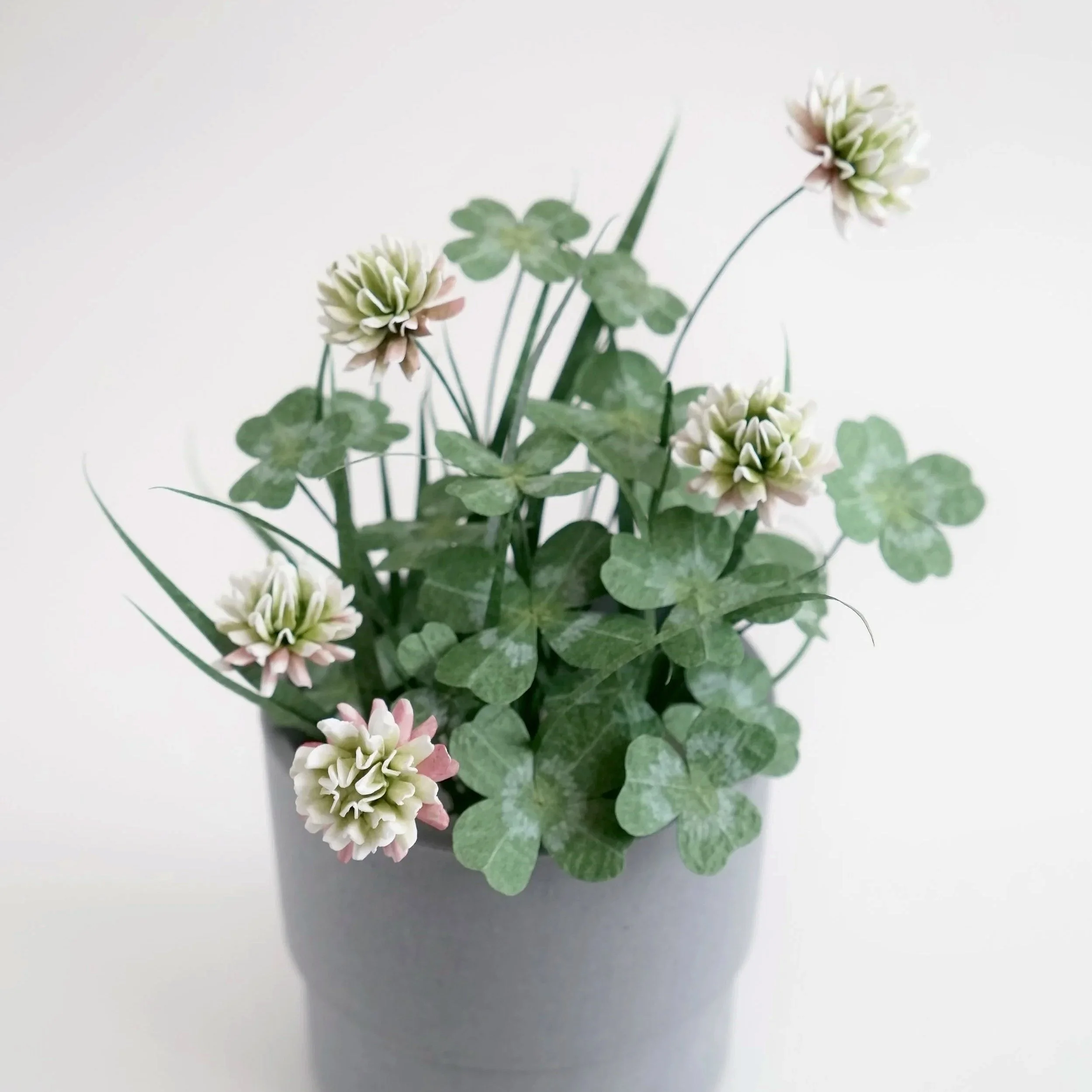 Close-up of a realistic potted plant with white and pink flowers and green leaves against a plain white background handmade by Jasmine Sing, paper artist from Merremade.