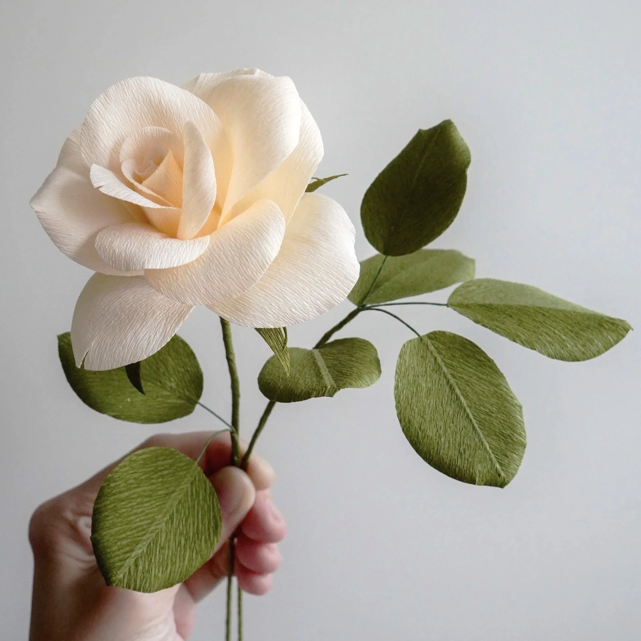 A realistic paper rose stem with several green leaves handmade by Jasmine Sing, paper artist from Merremade.