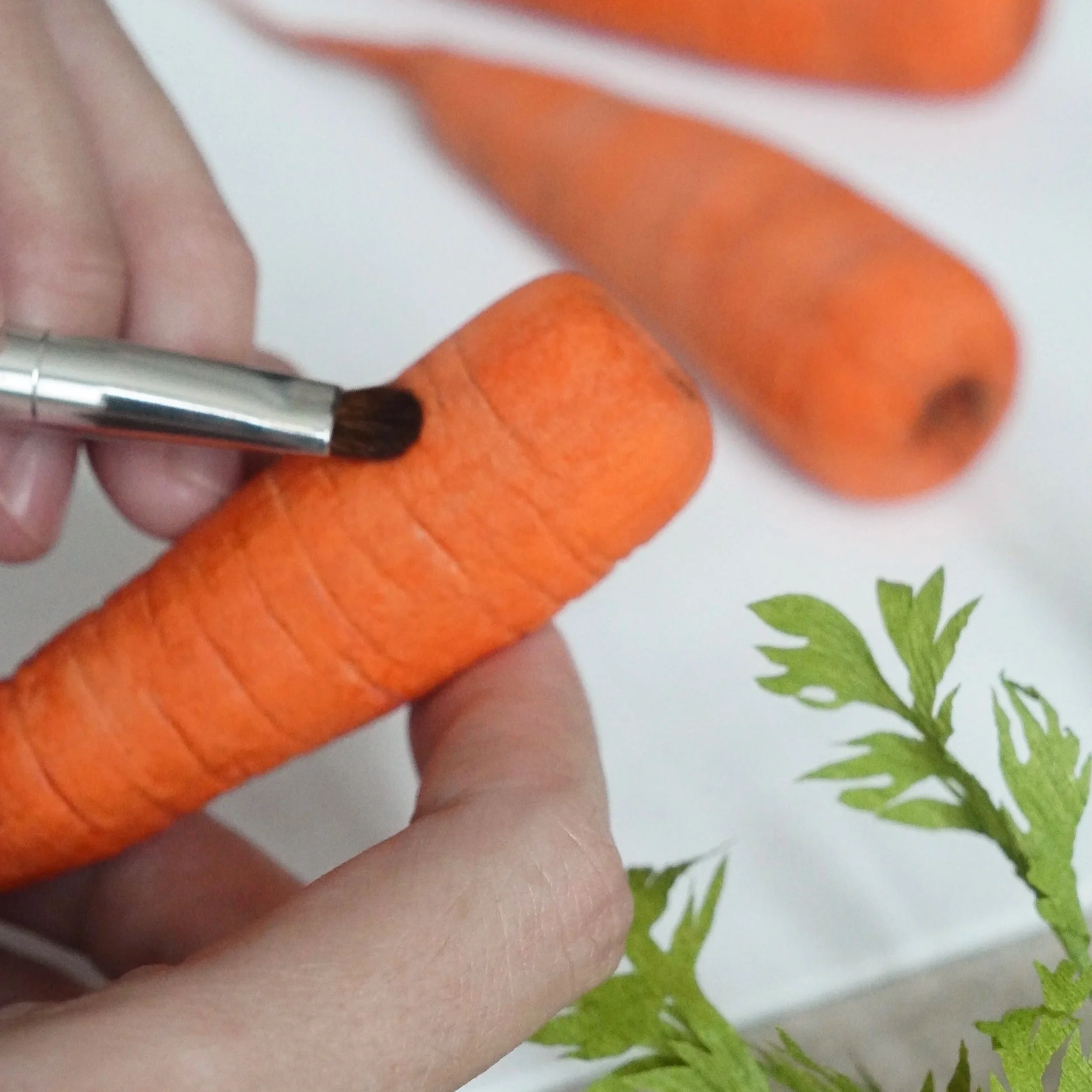 Close-up of a hand holding painting handmade paper carrots. online class preview.