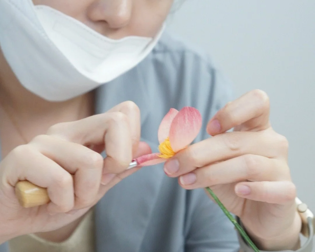 Merremade student holding a delicate pink and yellow flower, carefully arranging its petals during workshop in Seoul Korea.