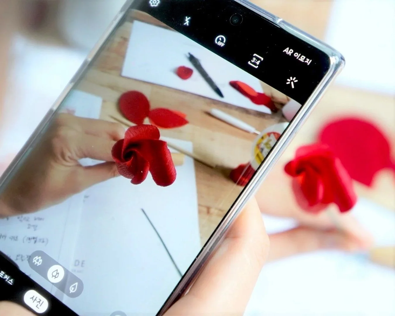 Merremade student taking a process photo of red paper flowers on a smartphone during Seoul Korea workshop.