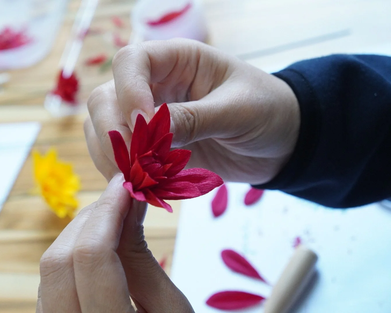 Merremade student arranging red paper dahlias with tools.
