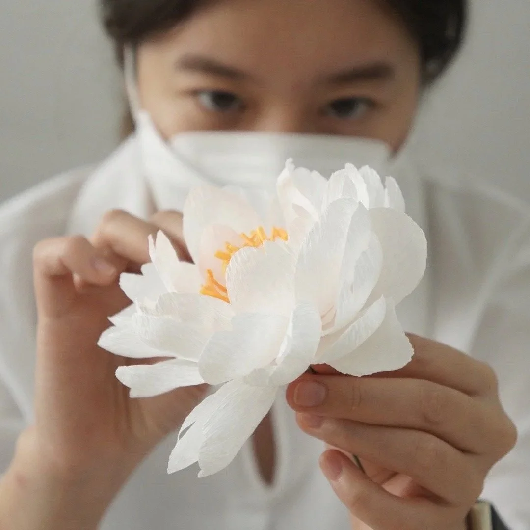 Merremade student holding a large handmade white paper peony with yellow and orange details inside during in-person workshop in Seoul Korea.