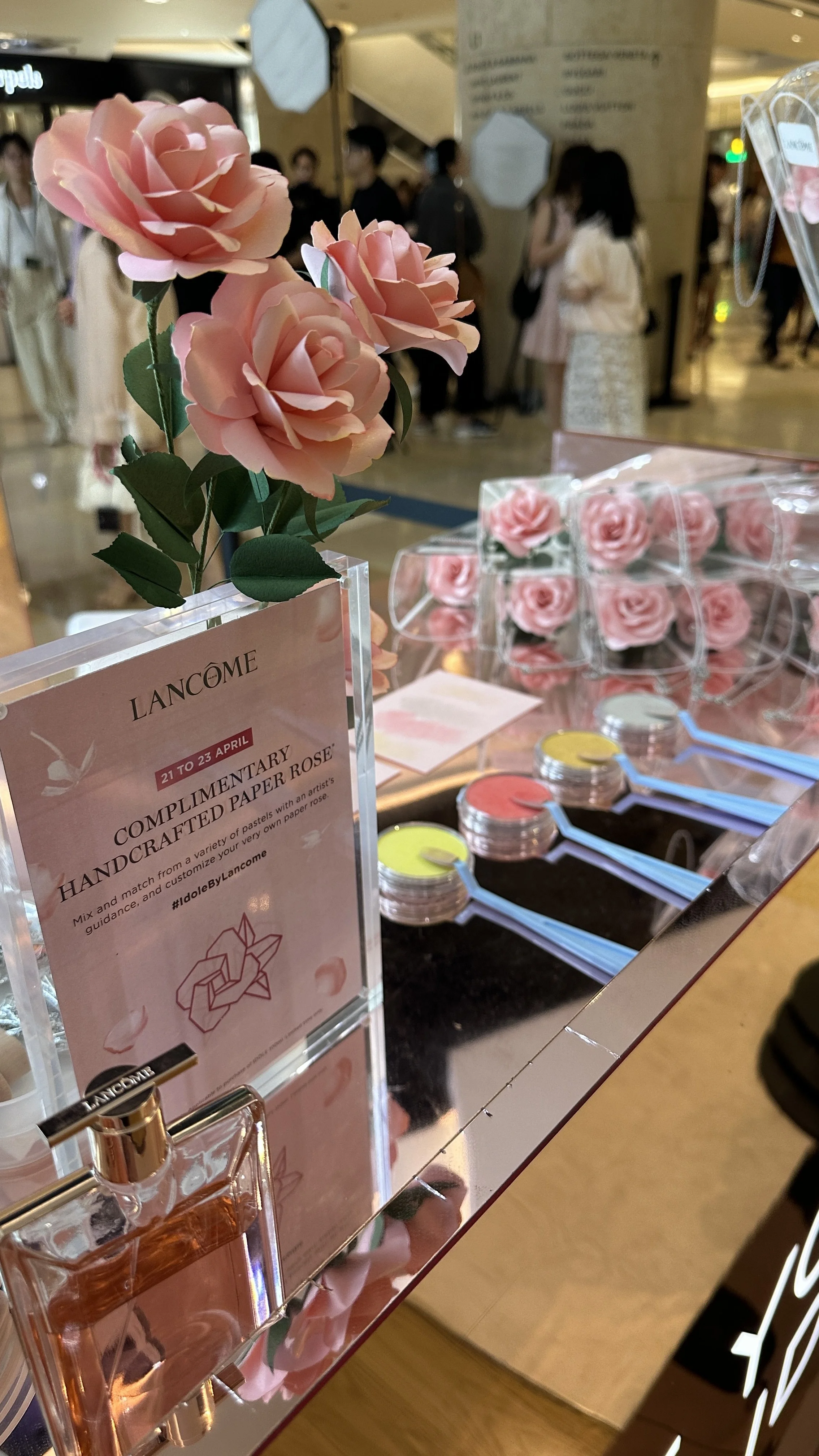 Pink paper roses and Lancome skincare products displayed at a Lancome event booth.
