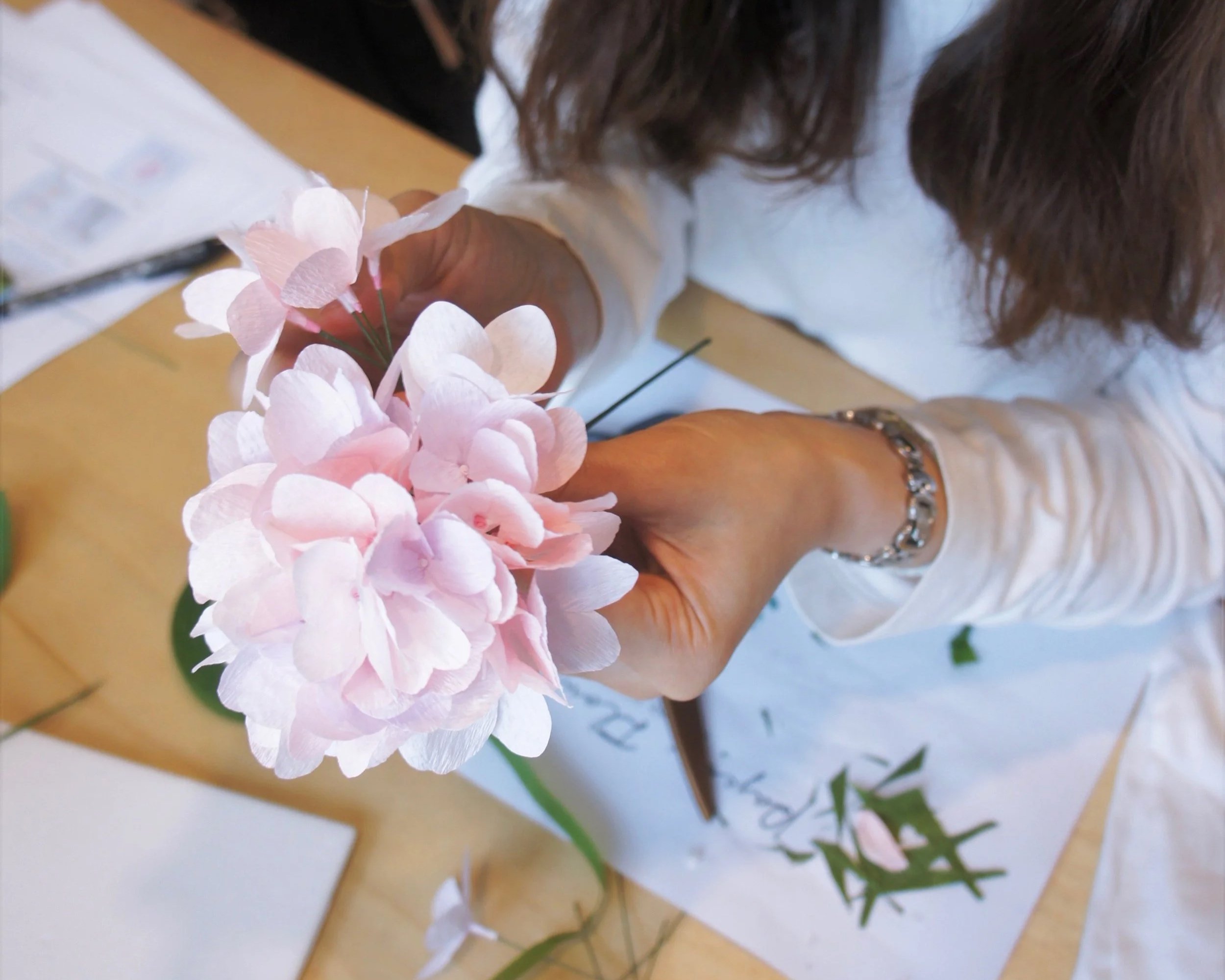 Merremade student making pink paper hydrangea flowers.