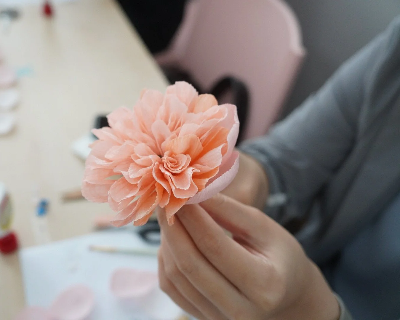 Merremade student holding a handcrafted peach-colored paper flower with layered petals.