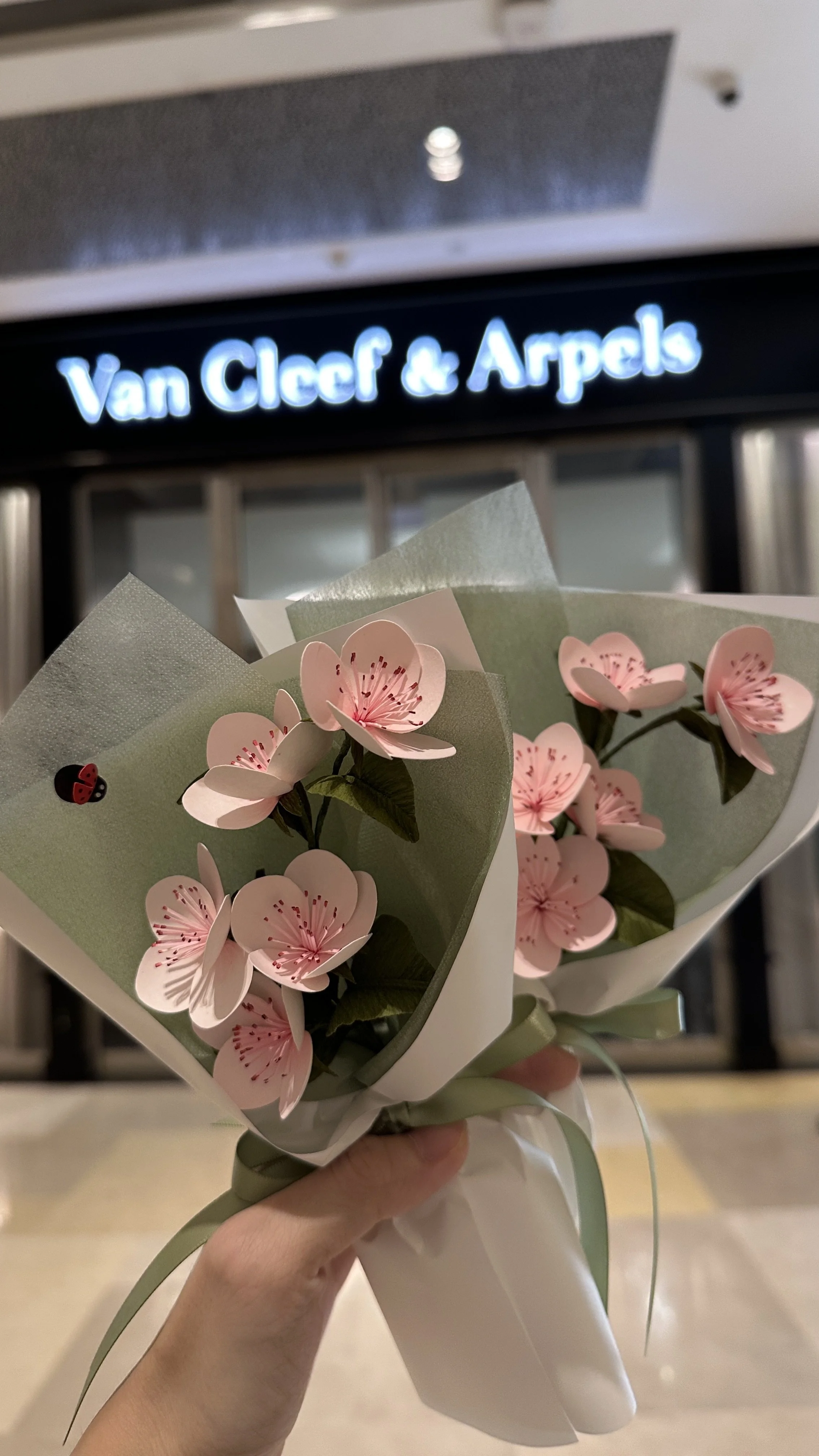 A bouquet of pink handmade realistic paper flowers in front of the Van Cleef & Arpels Singapore store sign.