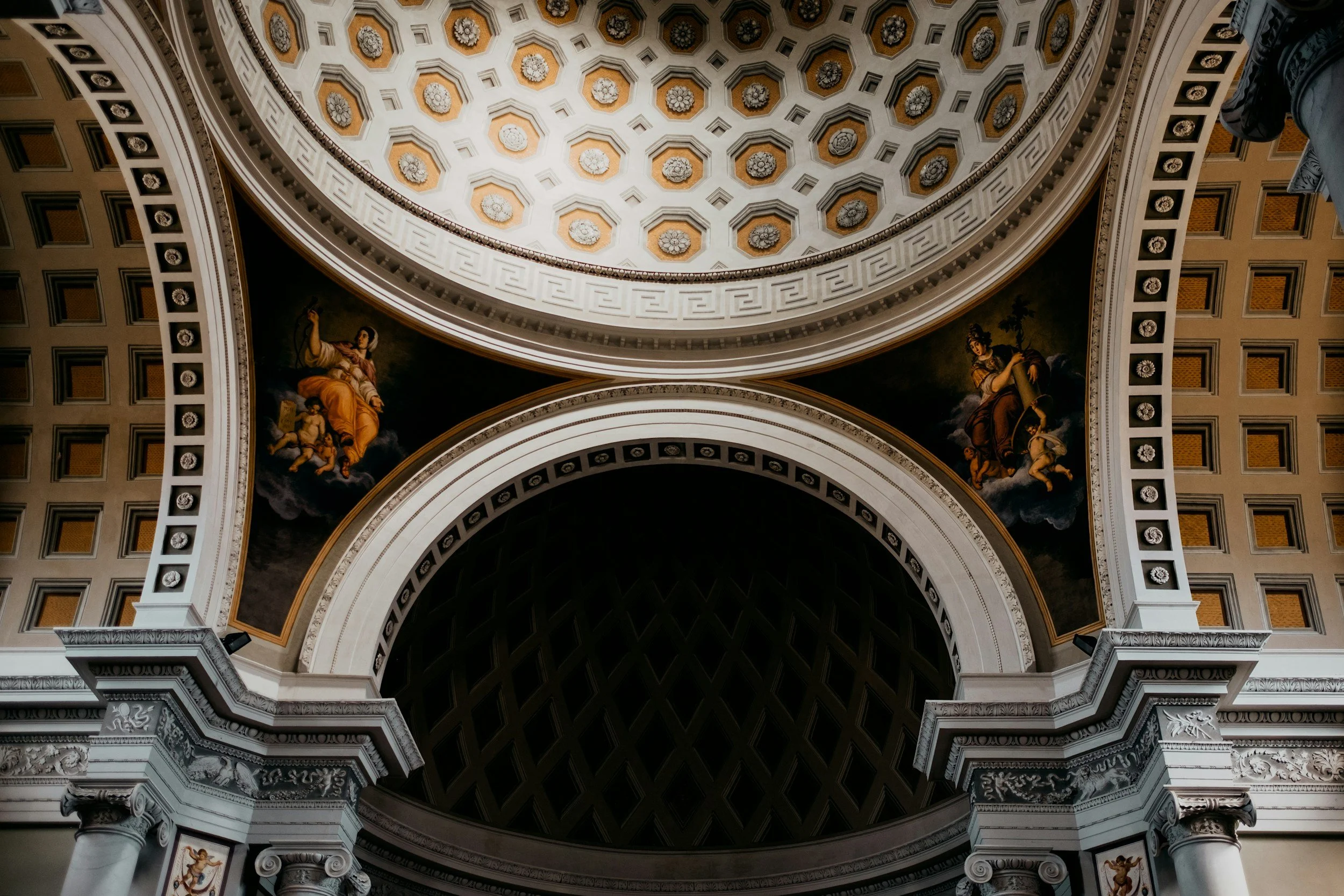 Interno di una grande cupola con motivi geometrici e decorazioni con figure dipinte ai lati, colonne e archi decorativi.