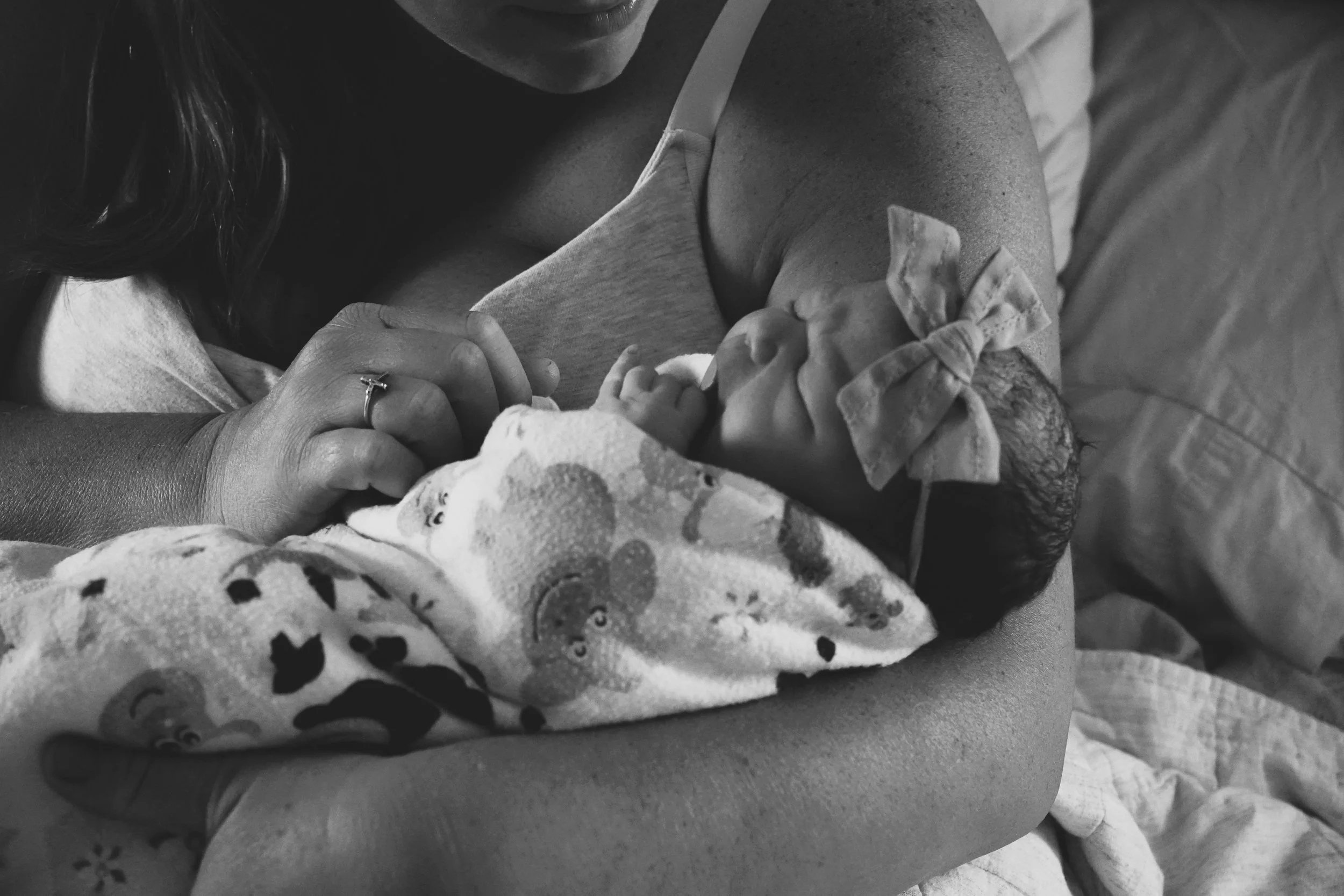 Close-up of a woman holding a baby. The woman is smiling and wearing a ring. The baby is wrapped in a blanket with animal prints.