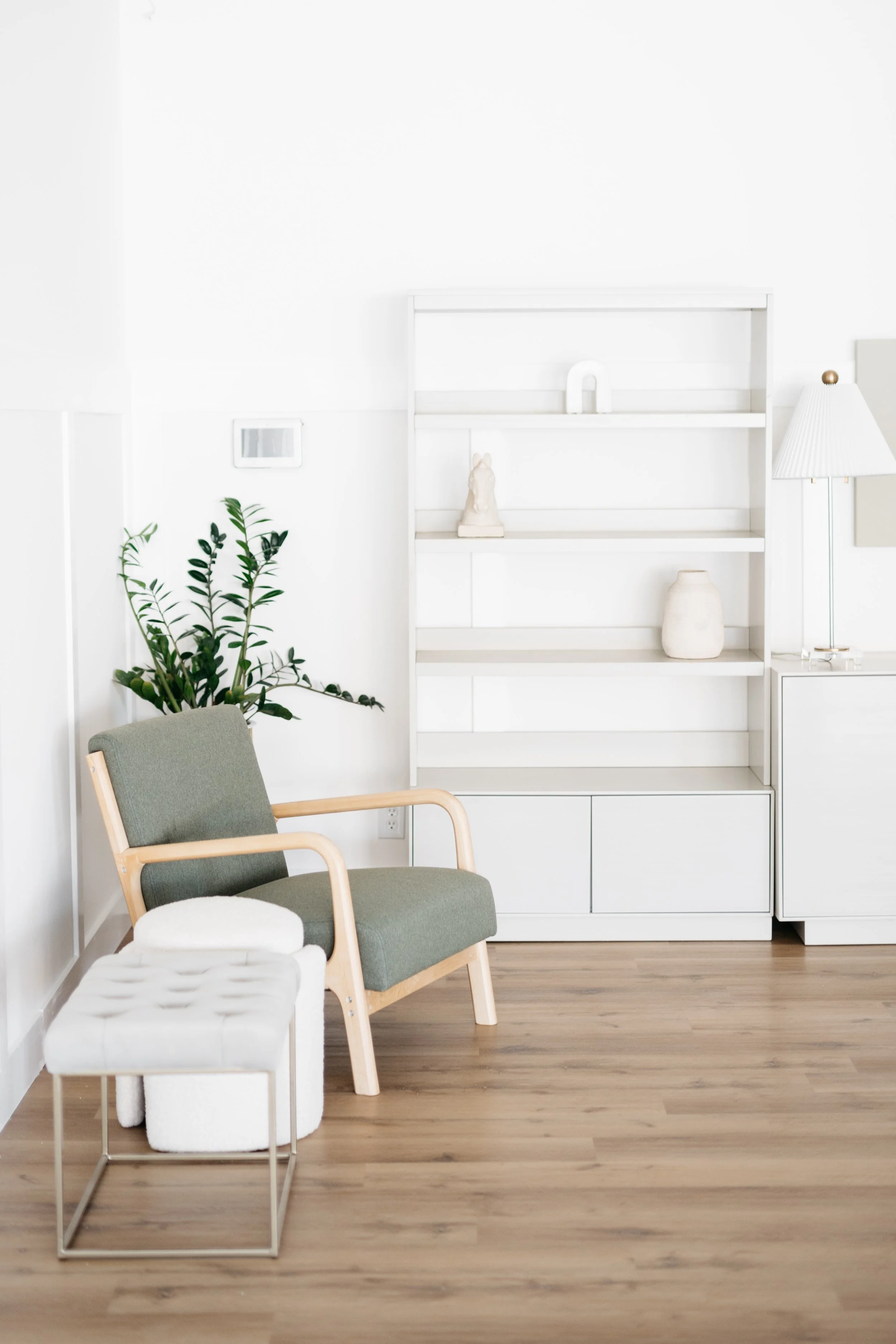 A minimalist office vibe with various chairs to fit your aesthetic or mood, bookshelves with decorative items, and live plants, featuring all neutral tones and wooden flooring.