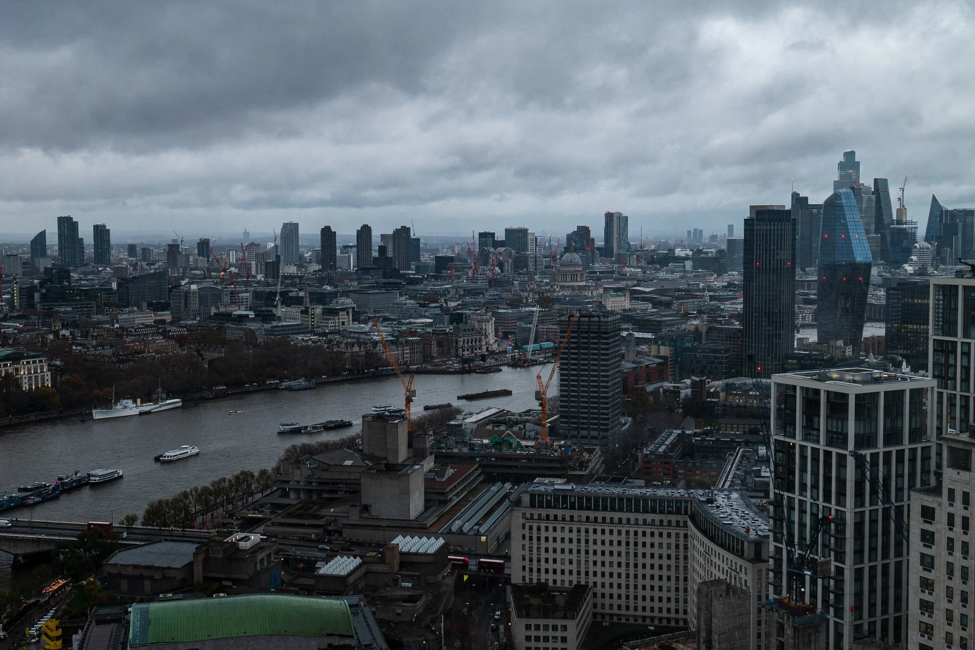 Panoramic view of London skyline with river and modern skyscrapers under cloudy sky.