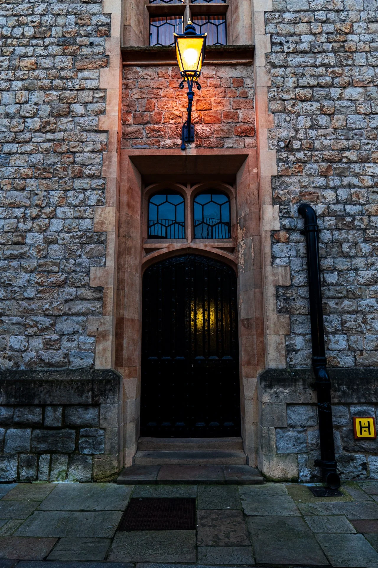 Old stone building with arched wooden door, illuminated by a lantern, and a cobblestone path.