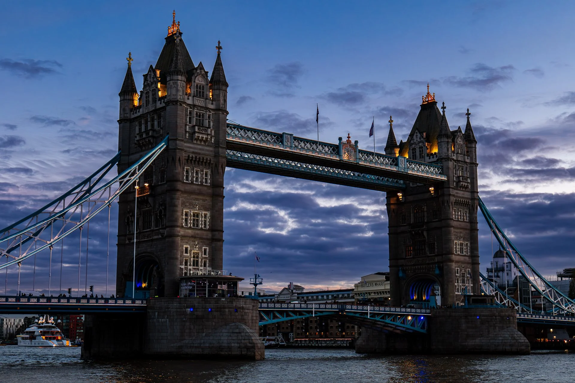 Tower Bridge in London at dusk, illuminated with a blue sky and clouds in the background.