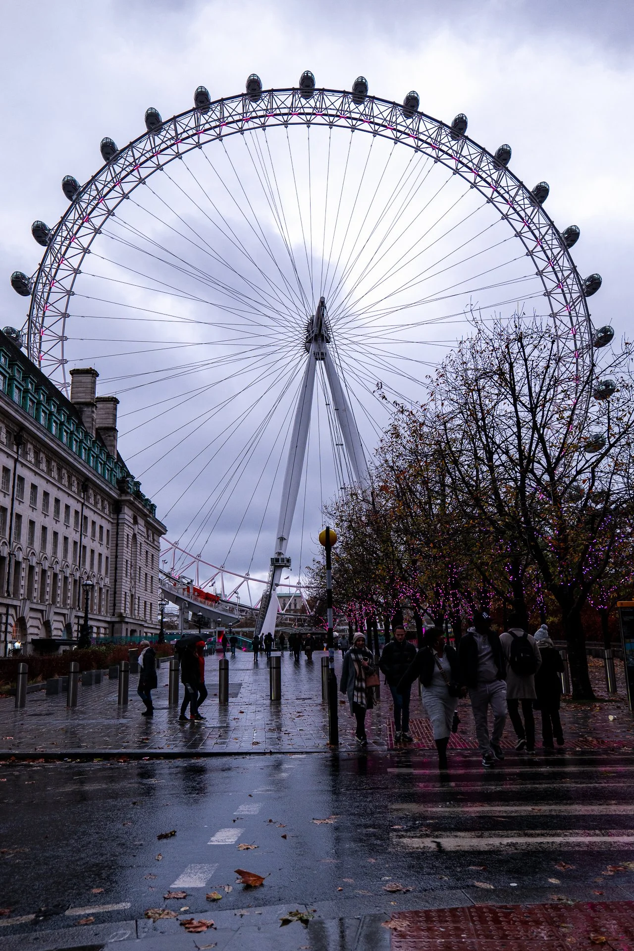 London Eye Ferris wheel on a cloudy day with people walking by.