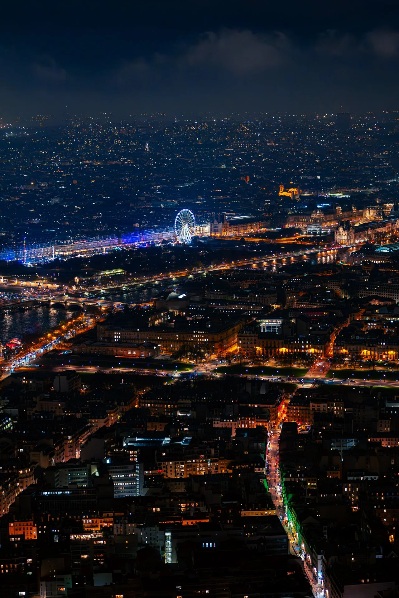 Aerial view of Paris at night, featuring a brightly lit Ferris wheel and illuminated streets.