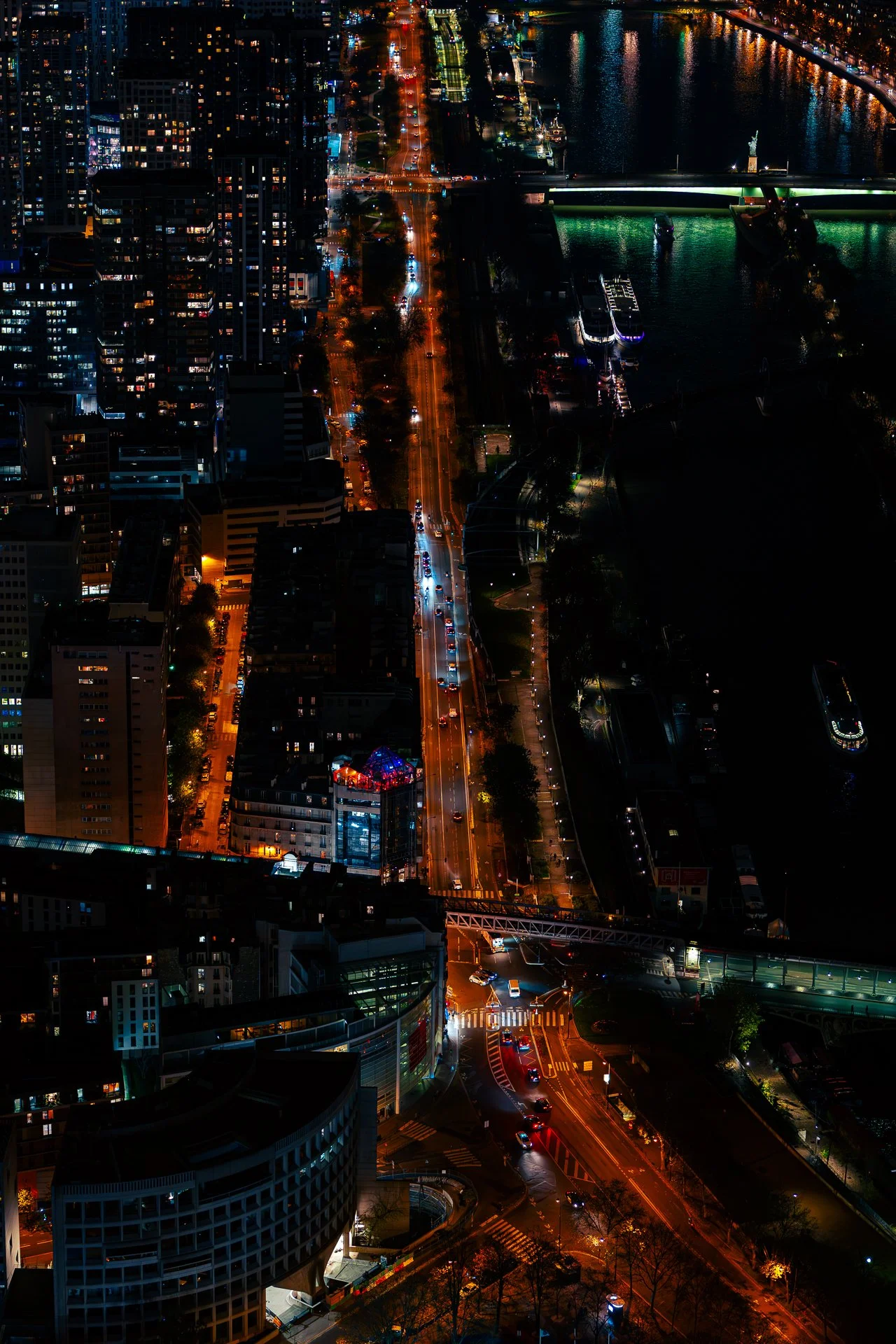 Aerial night view of a cityscape with illuminated streets, a river with bridges, and high-rise buildings.