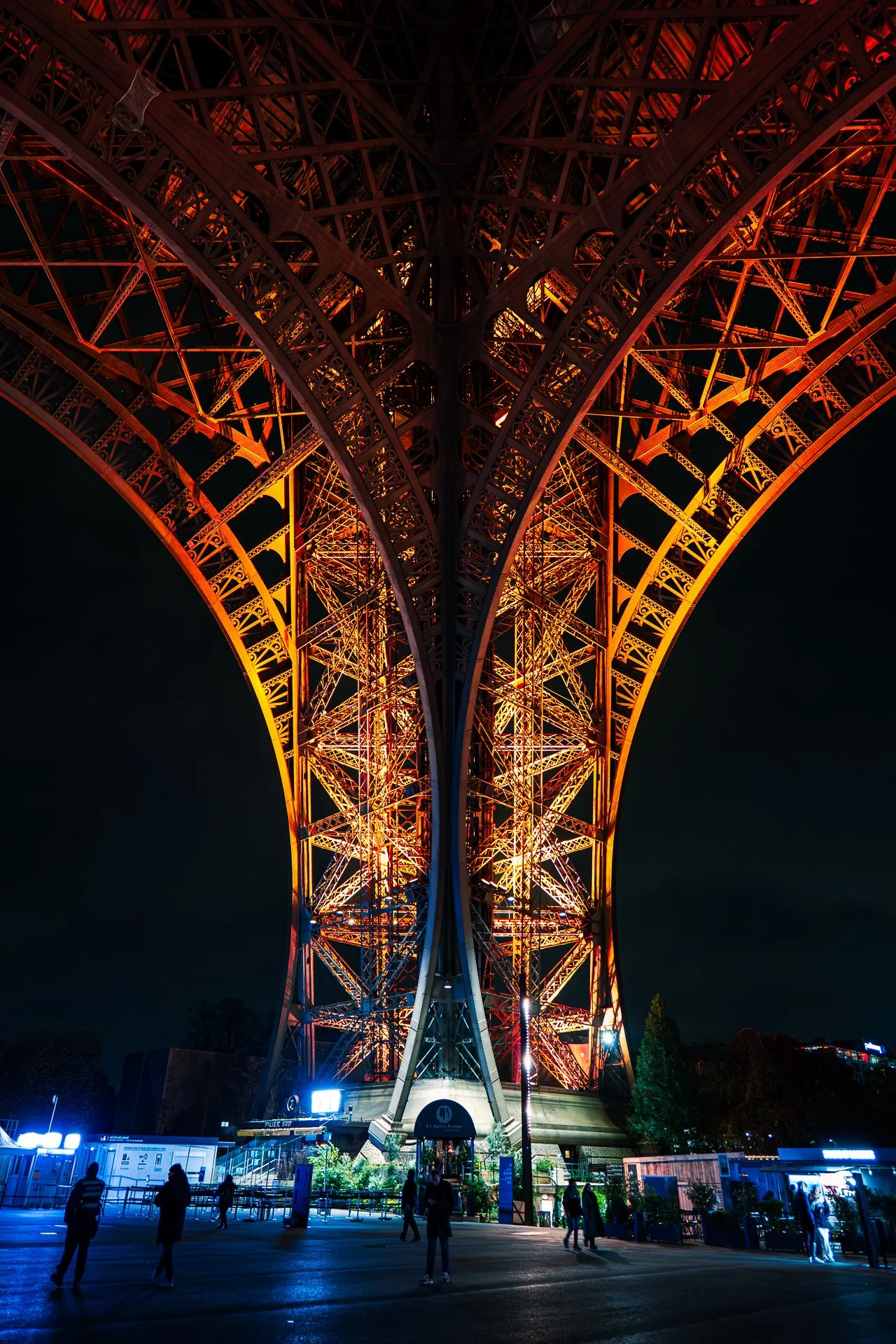 Illuminated structure of the Eiffel Tower at night with people walking underneath.