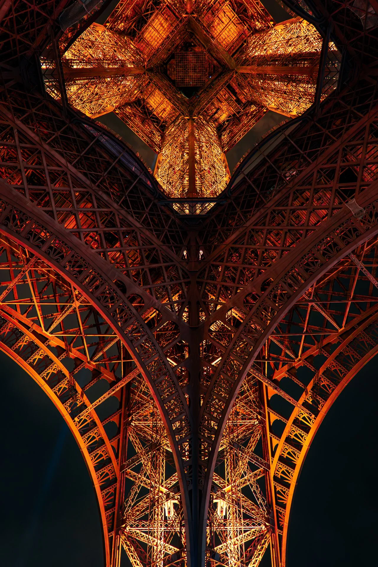 View from beneath the Eiffel Tower at night, showcasing its illuminated iron lattice structure.