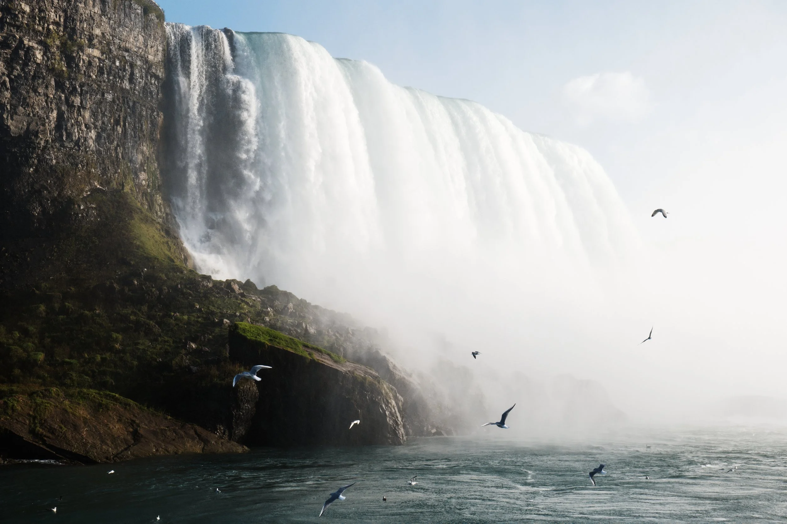 Large waterfall cascading over a cliff with mist and birds flying above the water surface.