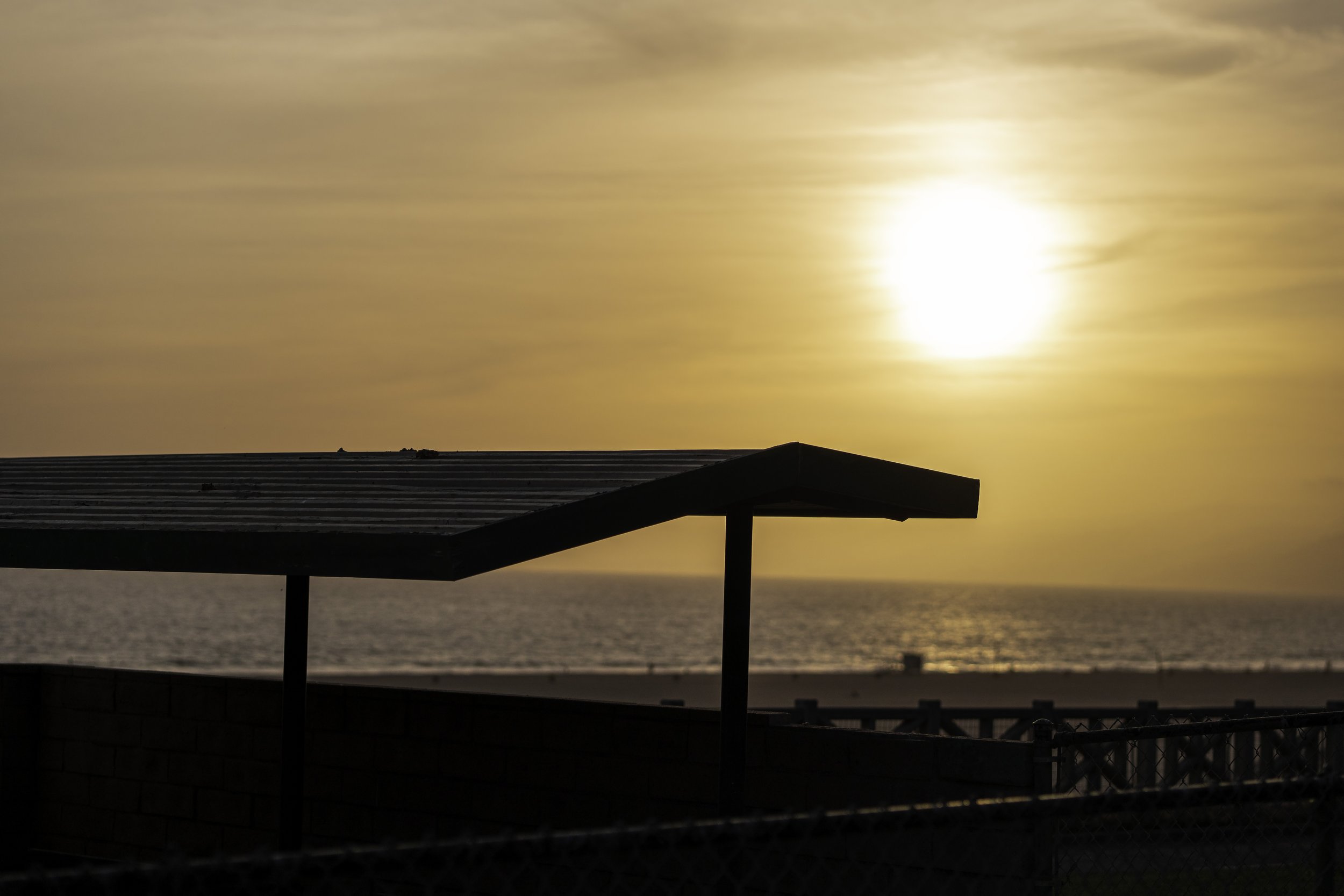 Silhouette of a pavilion roof at sunset by the ocean.