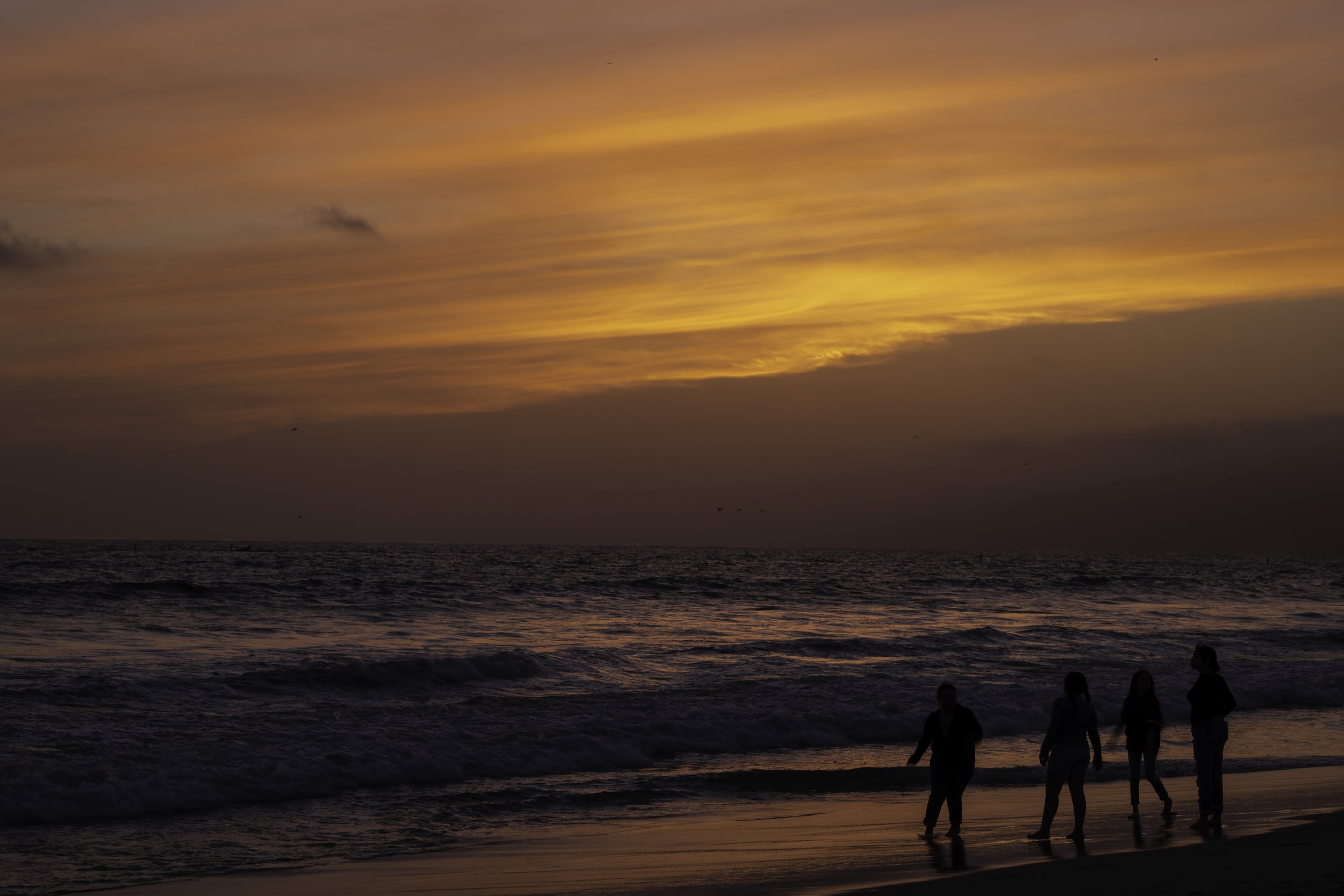 Silhouettes of people walking along a beach at sunset, with a colorful sky and ocean waves.