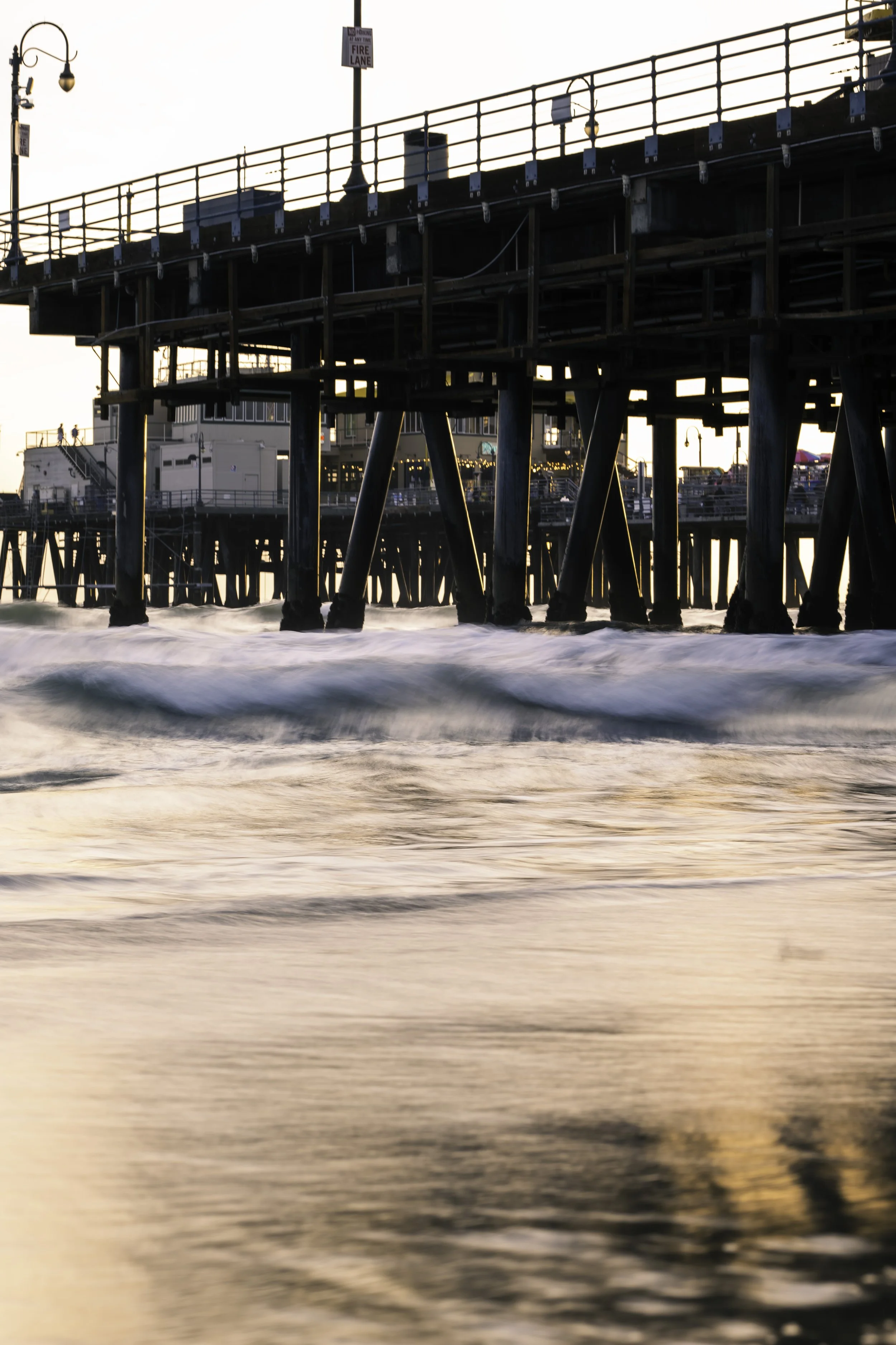 Ocean waves under a pier at sunset