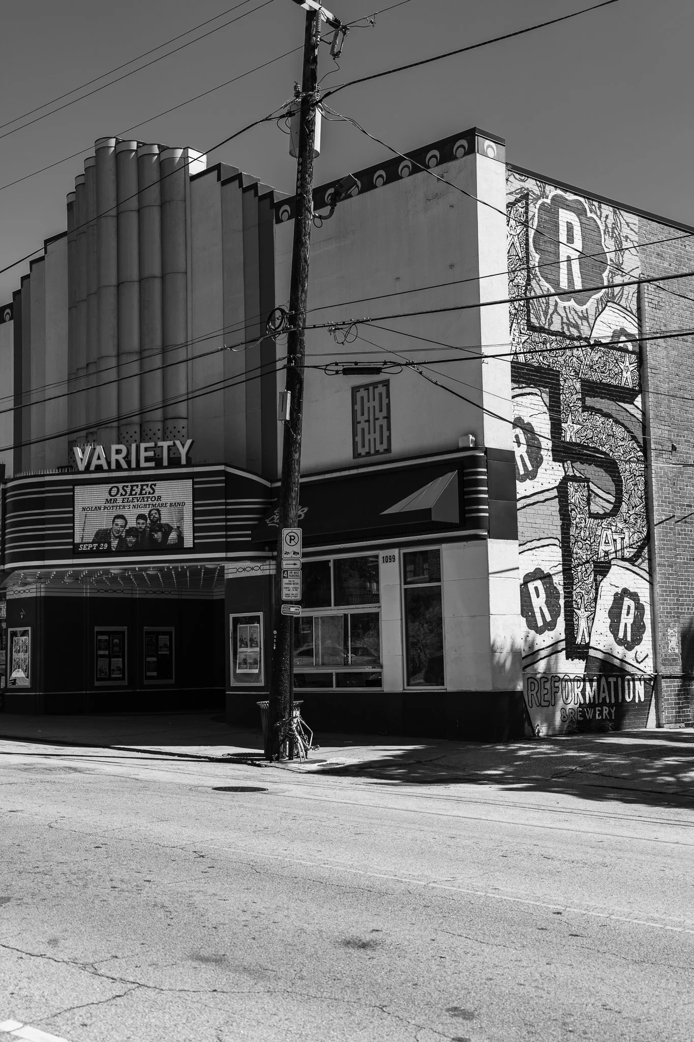 Black and white photo of an art deco theater building named Variety, featuring a marquee with show information and large mural advertising Reformation Brewery on the side. Power lines and a utility pole are visible in the foreground.