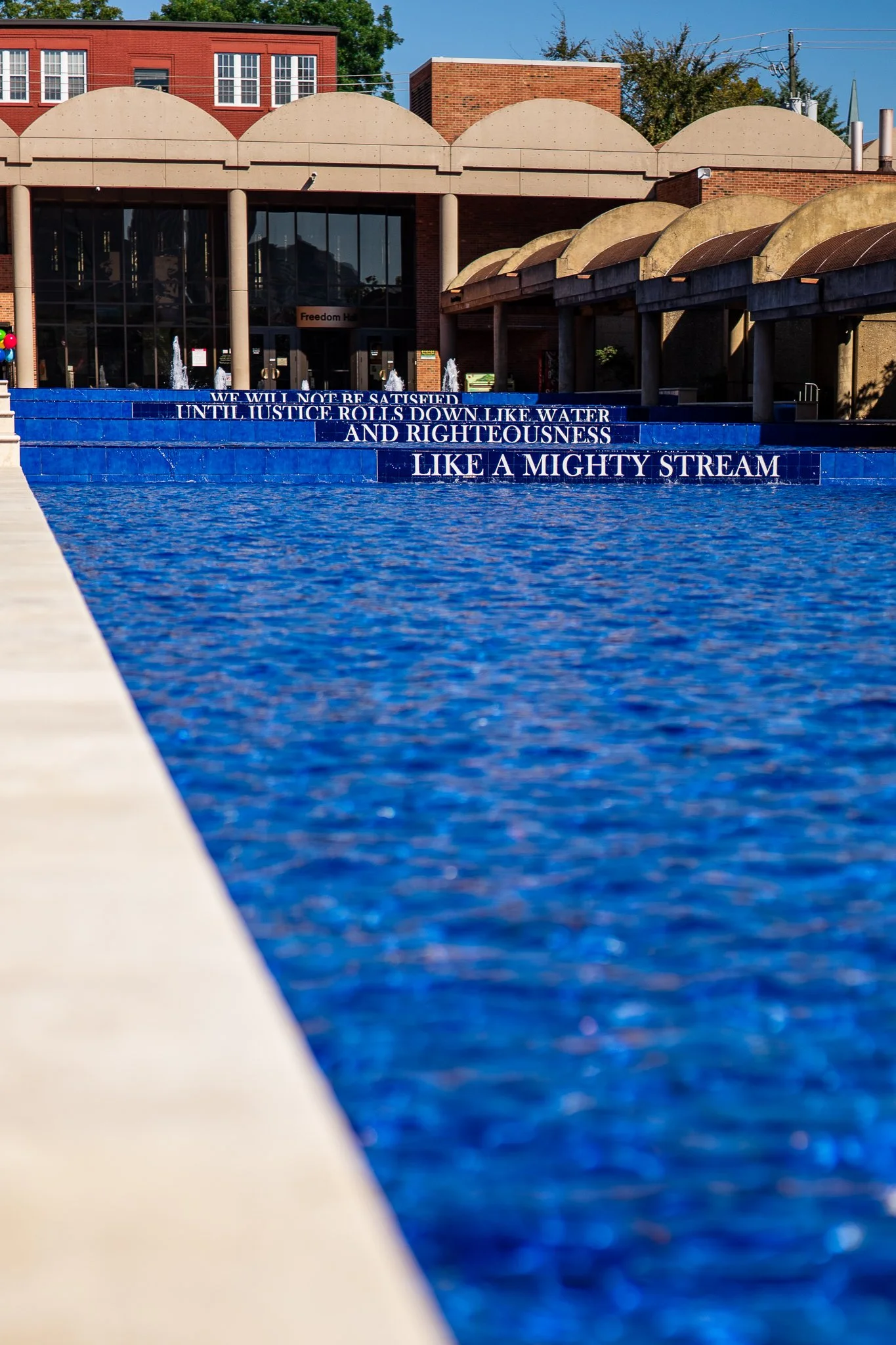 Reflecting pool with quote on steps, red brick building in background.