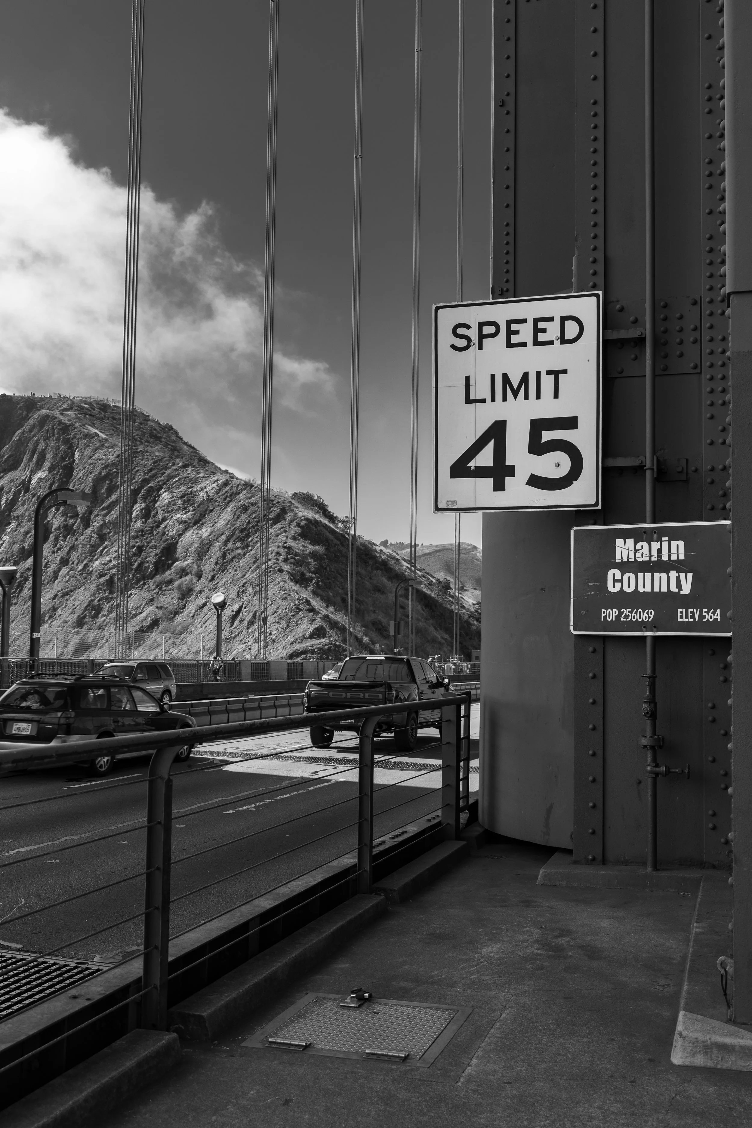 Black and white photo of a bridge with vehicles crossing, featuring a Speed Limit 45 sign and a Marin County sign.