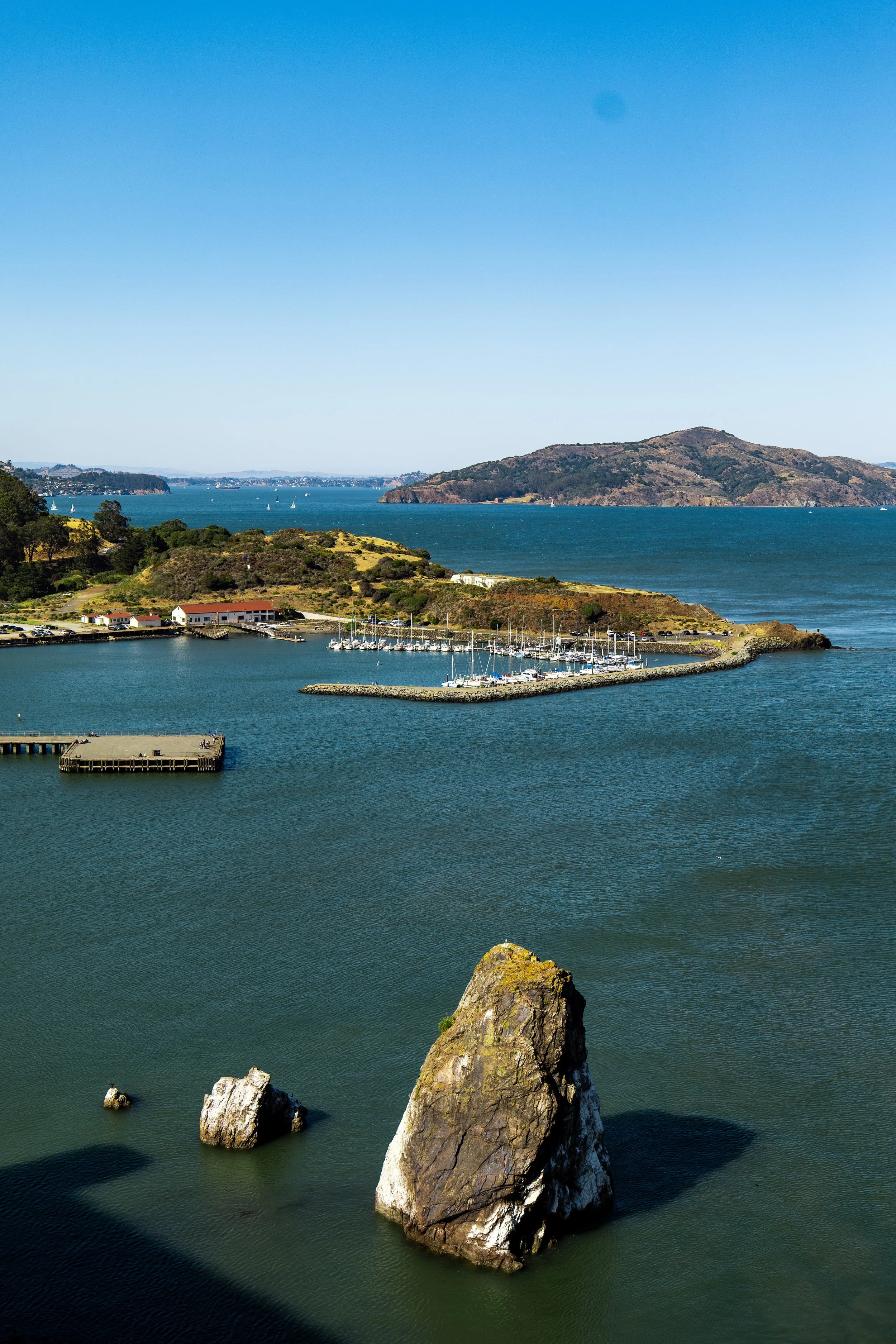 Aerial view of a coastal landscape with a marina, rocky shores, and a small island in the background.