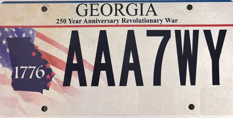 Novelty Georgia license plate celebrating the 250th anniversary of the American Revolution, featuring the year 1776, the abbreviation AAA7WY, and patriotic design elements.