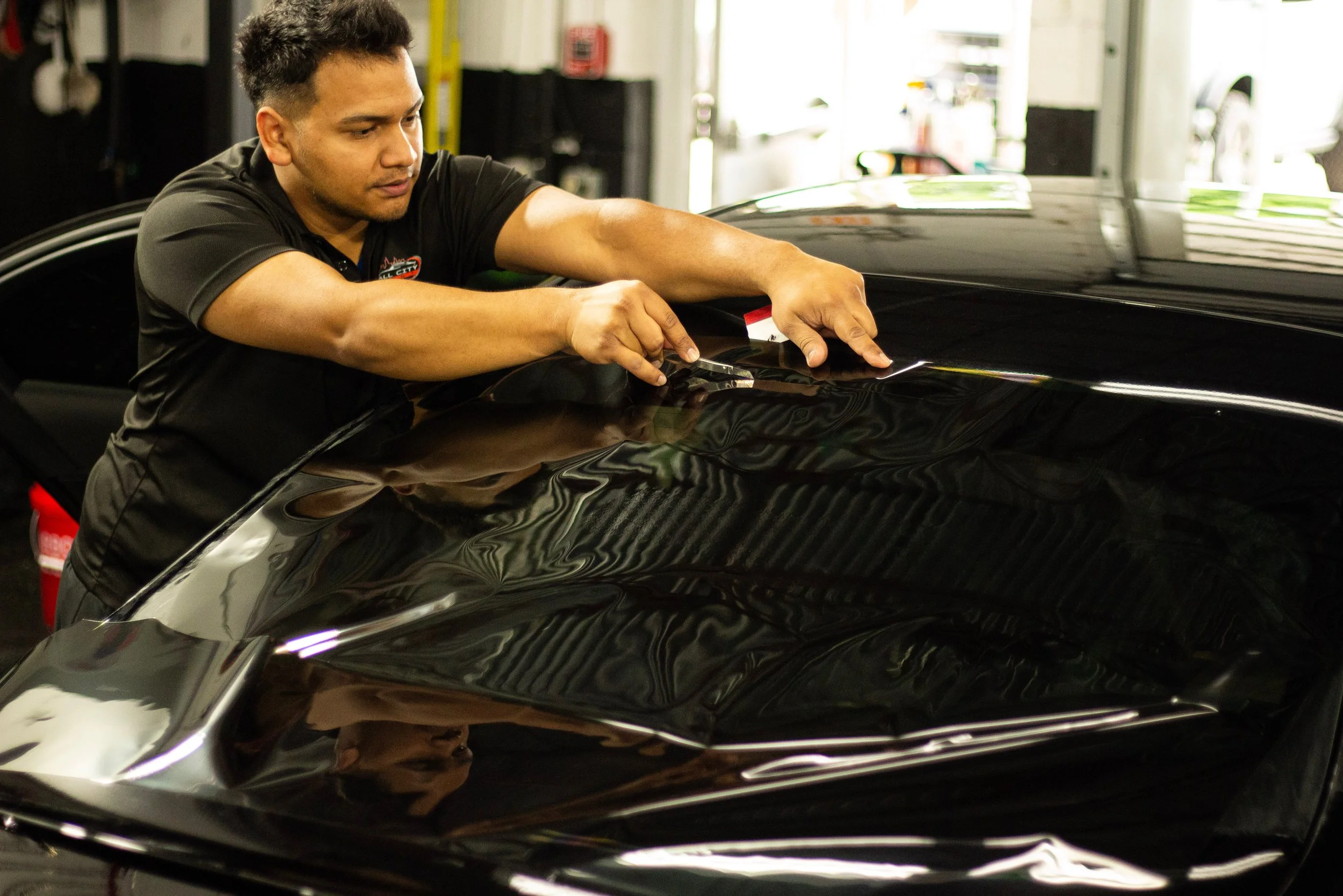 A man working on a black sports car in a garage or workshop.