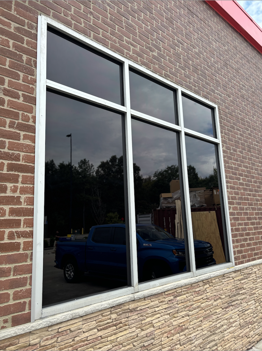 Reflection of a blue pickup truck and a cloudy sky in a large window of a brick building.